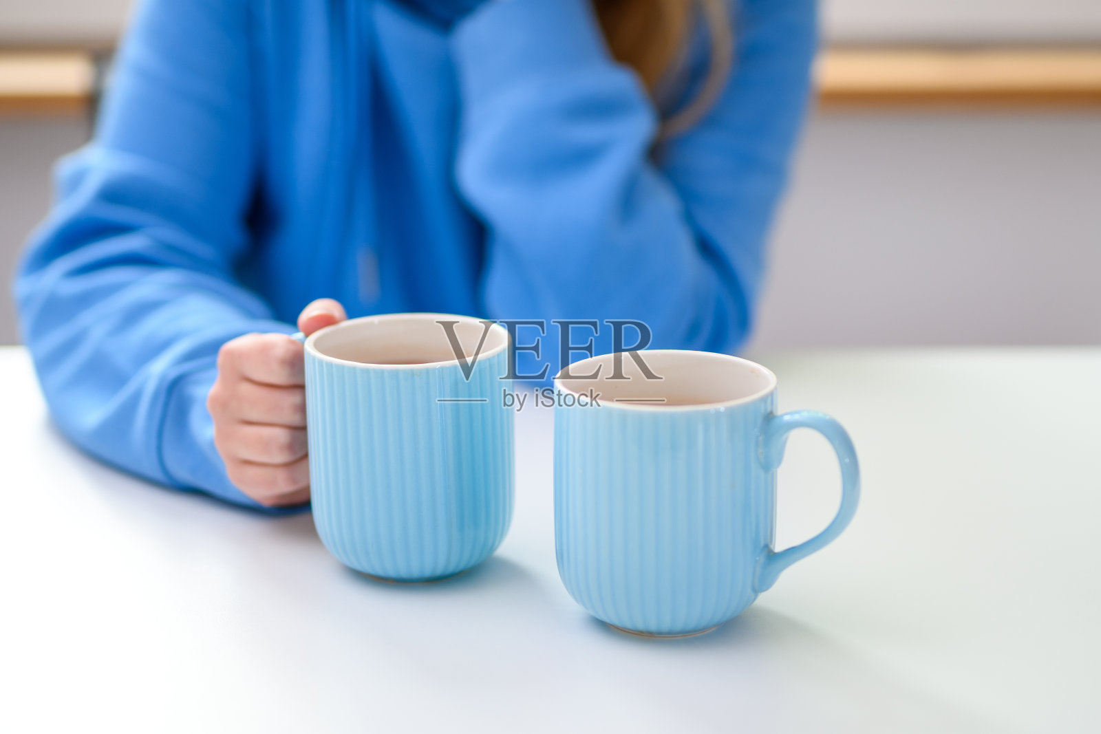 一个女孩正端着两杯茶坐在桌旁等着。照片摄影图片