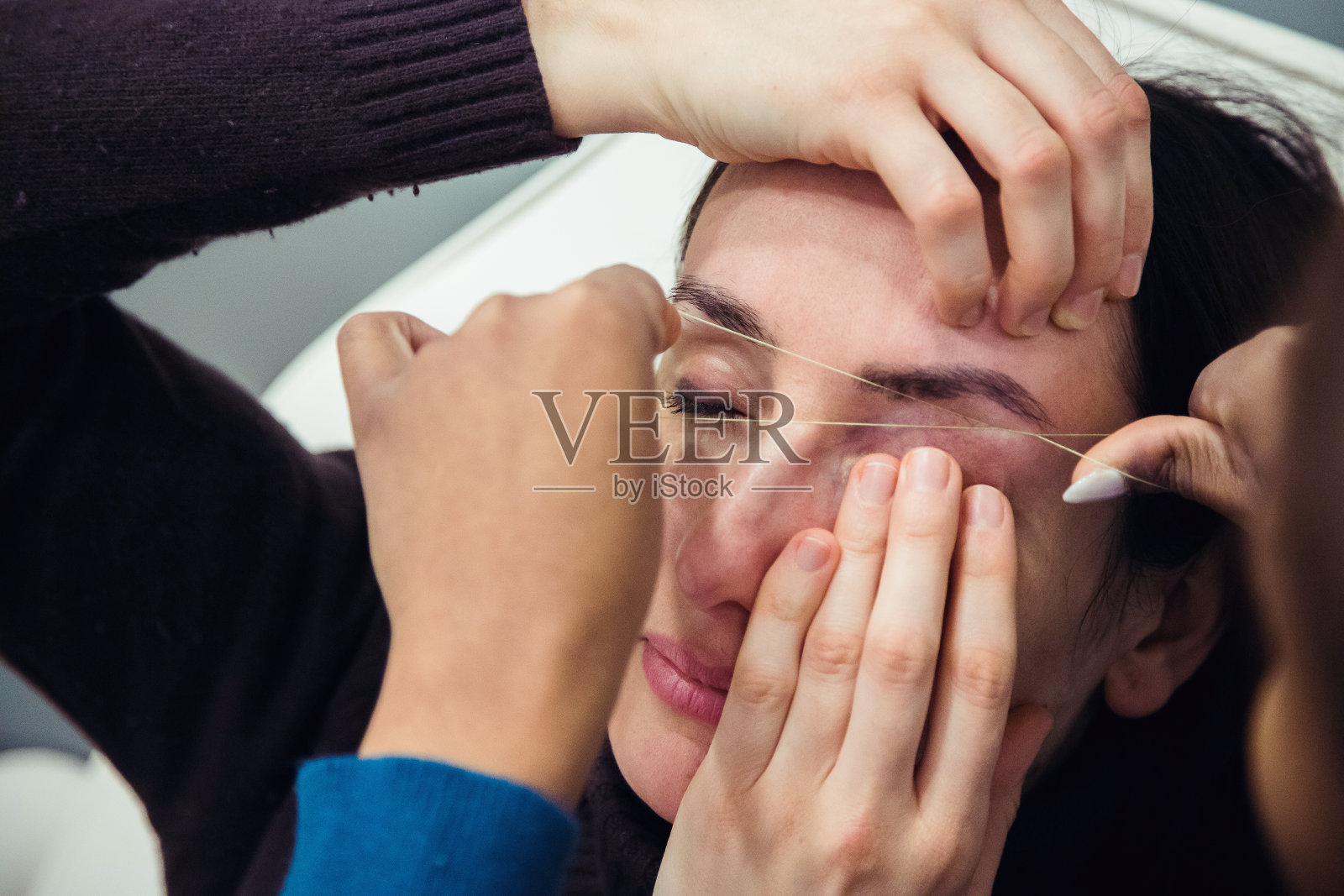 一名白人妇女正在用眉毛造型师的针线技术去除眉毛上的毛发。线程。流程步骤。近距离照片摄影图片