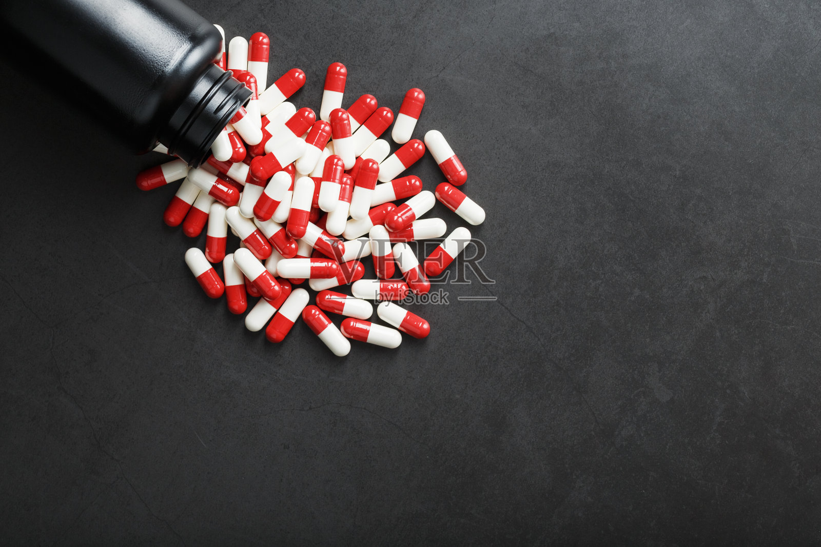 红色和白色药丸从一个黑色的罐子在黑色的背景。照片摄影图片