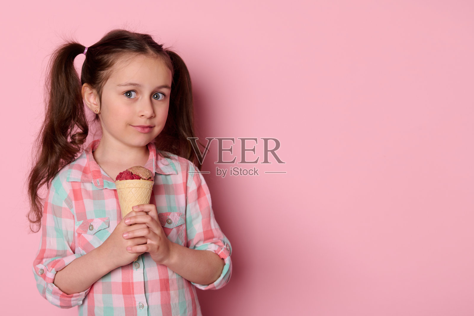 可爱的蓝眼睛小女孩微笑着看着镜头，拿着一个华夫蛋筒和冰淇淋，粉红色的背景照片摄影图片