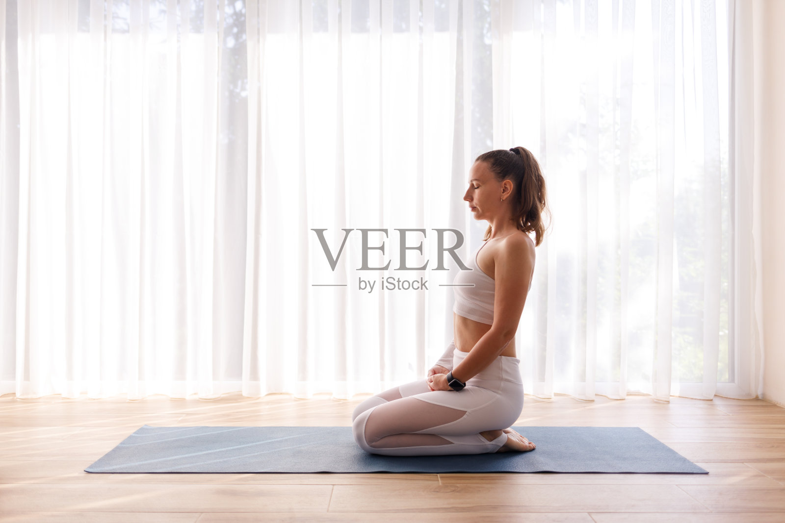 穿着白色运动服的年轻女子在大窗户旁边冥想照片摄影图片