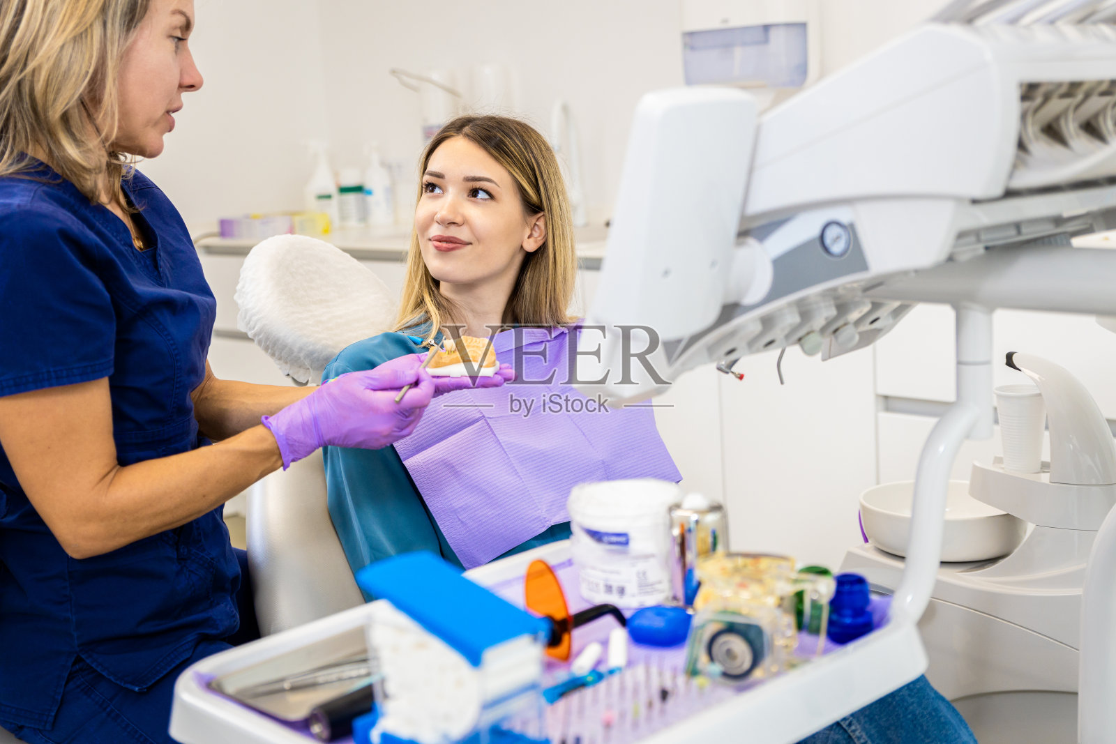 女牙医在牙科诊所与展示种植体的病人交谈。照片摄影图片
