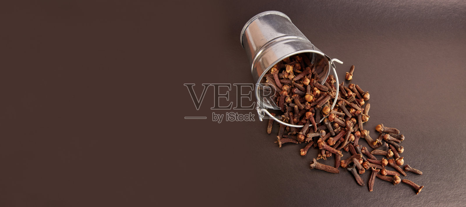 一个黑色背景的小金属桶，里面装满了丁香香料。照片摄影图片