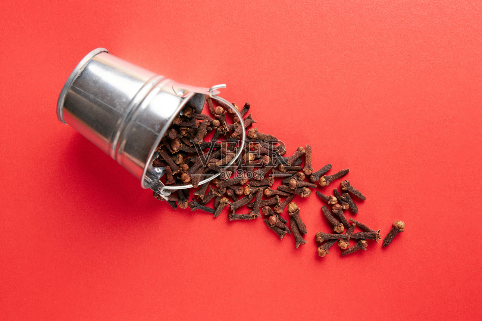 一个小金属桶，里面装满了红色背景的丁香香料。照片摄影图片