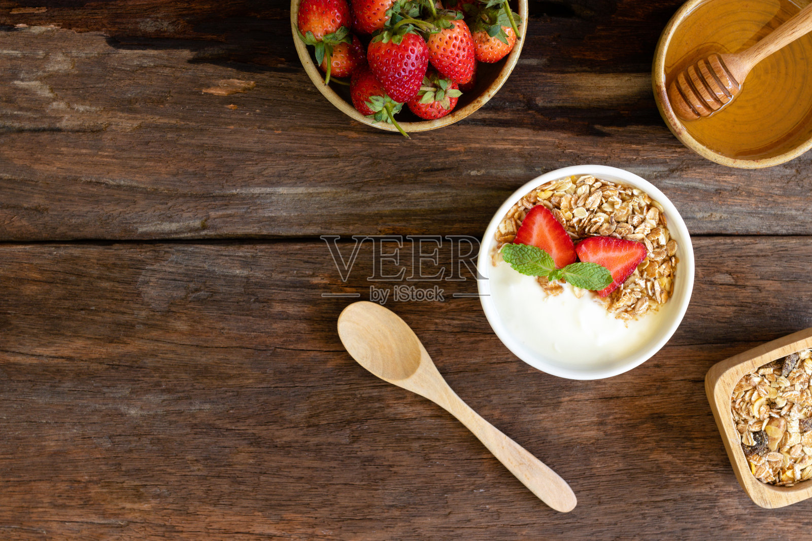 草莓酸奶装在木碗里，配以格兰诺拉麦片、薄荷和新鲜草莓。健康食品理念。照片摄影图片