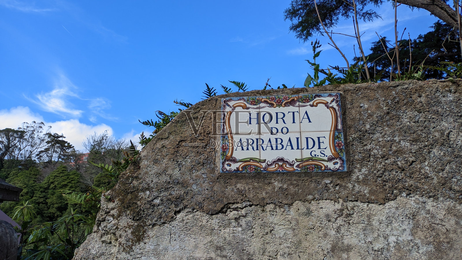 一座被毁坏的房子，只剩下一个写着街道名字的牌子:奥尔塔·阿拉瓦尔德G.S.，映衬着葡萄牙辛特拉的蓝天和自然照片摄影图片