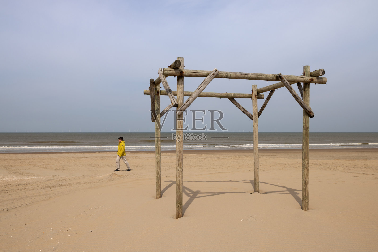 沙滩上孤零零的木凉棚，一个穿黄色夹克的男人走过。照片摄影图片