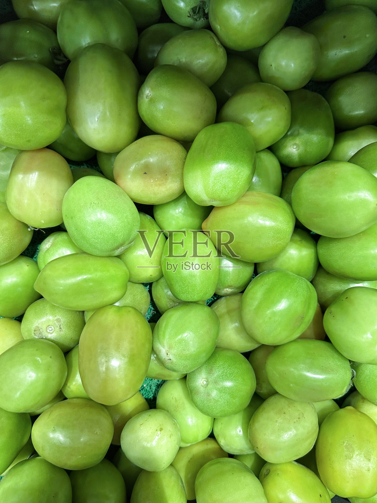新鲜农产品市场上一堆未成熟的绿色圣果(Solanum lycopersicum var. cerasiformme)的全画幅图像，高架视图，重点放在前景上照片摄影图片