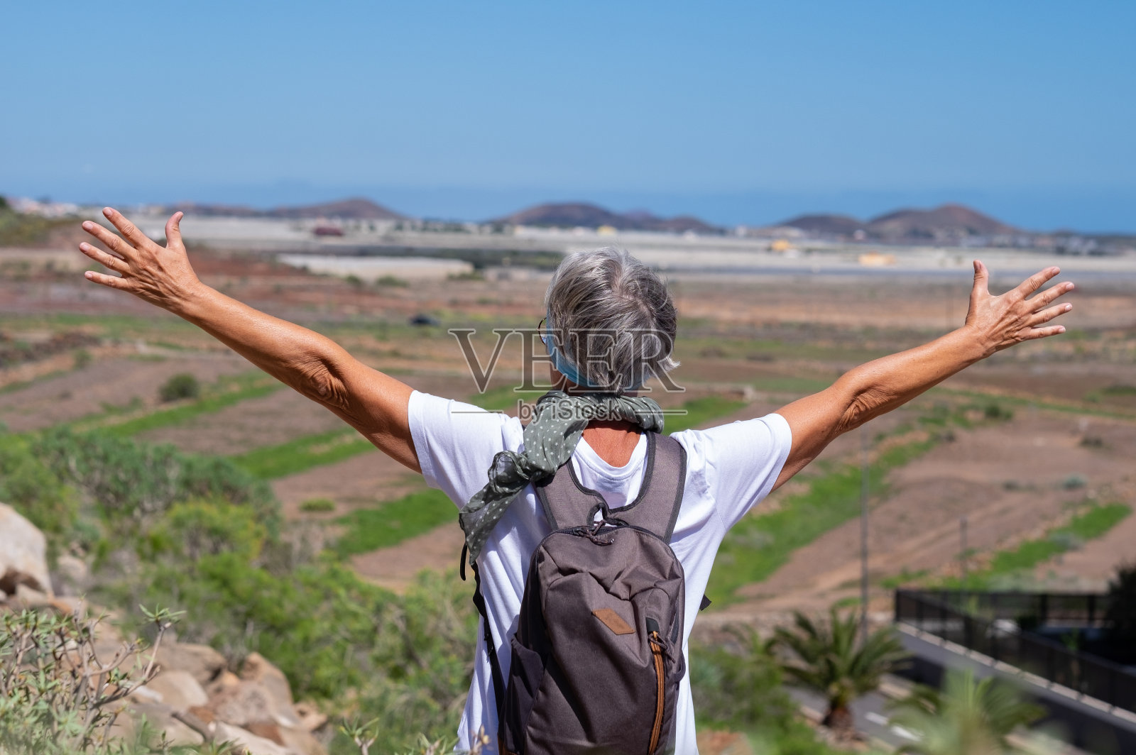 在户外远足的成熟老年妇女的后视图，伸开双臂望着地平线。在阳光明媚的日子里，白发苍苍的活跃女士在大自然中远足照片摄影图片