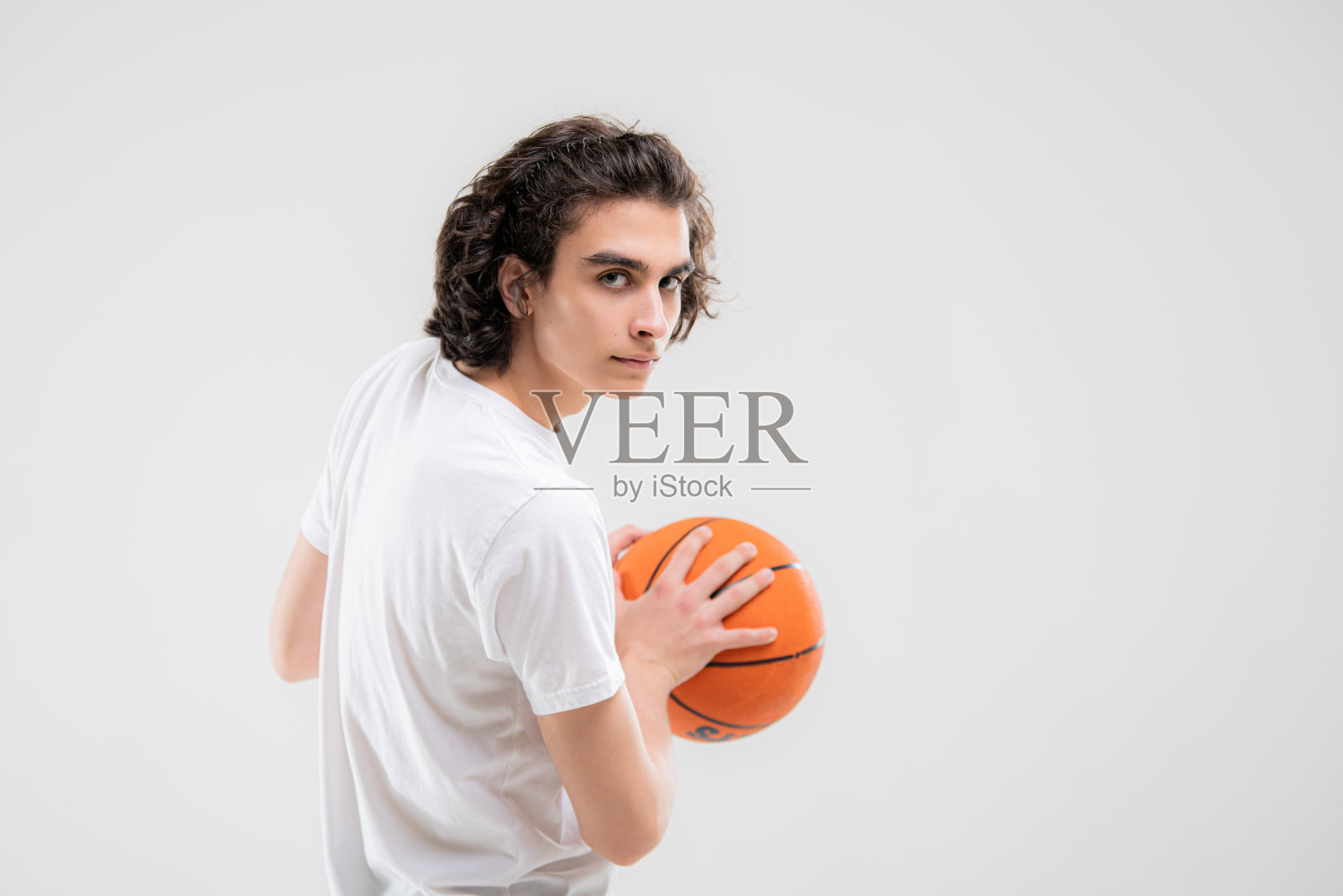 微笑的少年，篮球运动员在白色背景上拿着球摆姿势。照片摄影图片