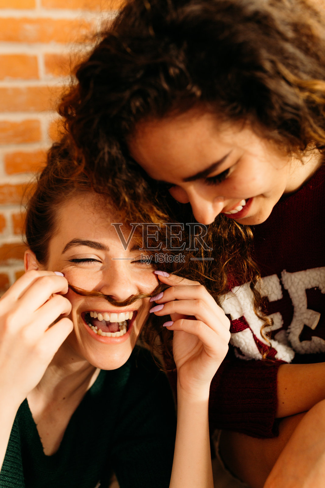 两个年轻的女人用头发弄胡子，一起笑得很开心照片摄影图片