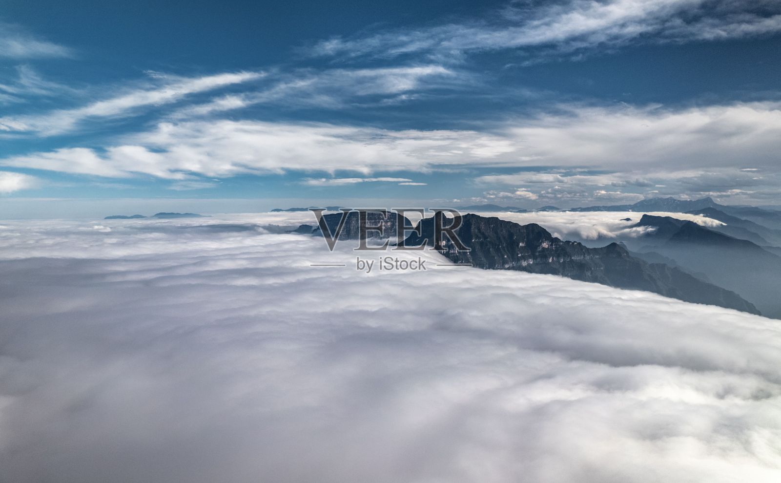 蓝蓝的天空下，云和雾覆盖着岩石山的景观照片摄影图片
