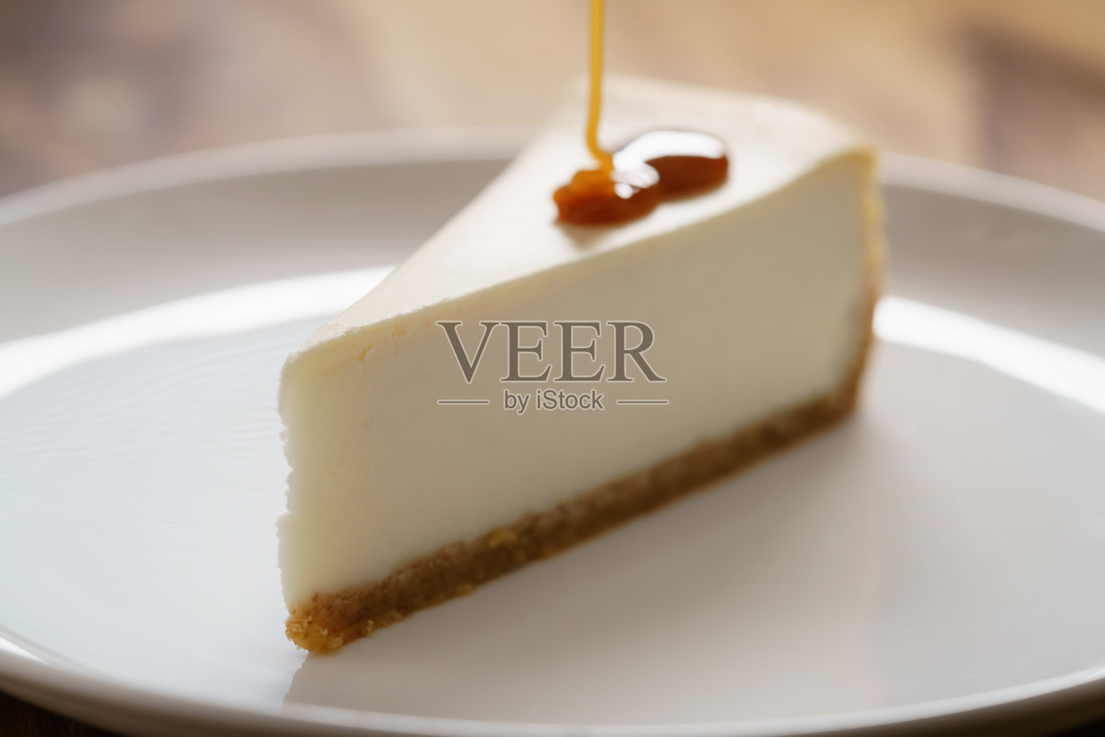 焦糖酱倒在一片传统的纽约芝士蛋糕上，放在木桌上的白色盘子里照片摄影图片