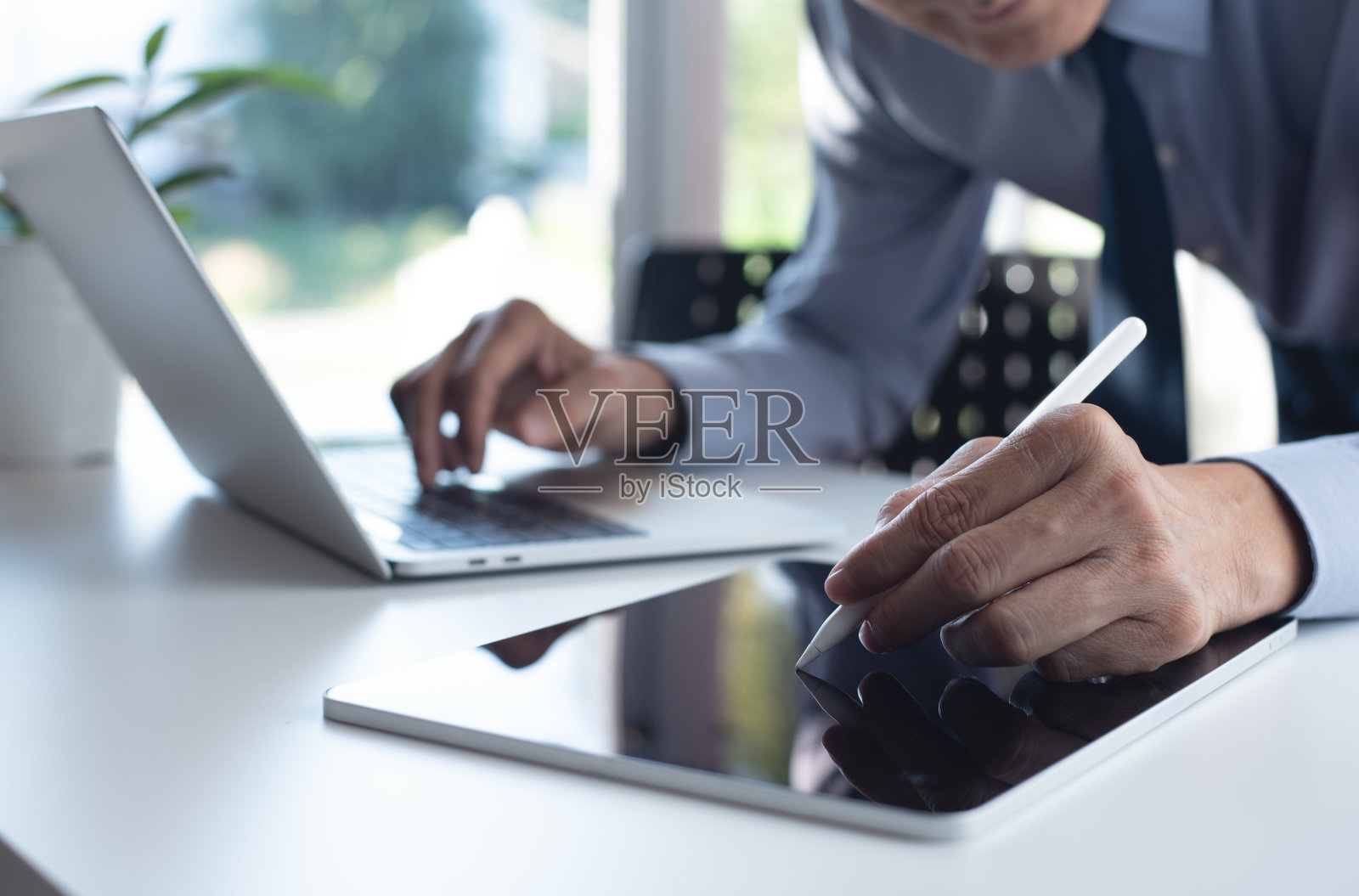 商人在办公桌上使用数码平板电脑和笔记本电脑。公司职员在平板电脑上使用手写笔校对和签署电子文件照片摄影图片