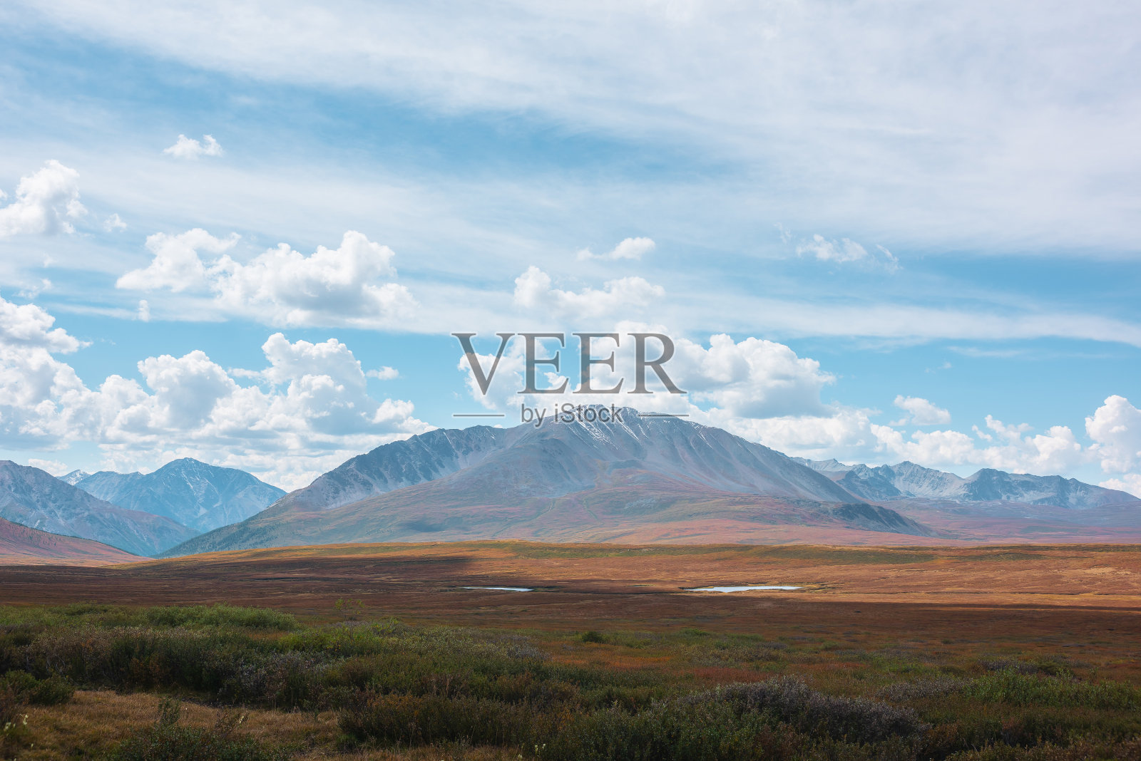 五彩缤纷的秋景，阳光明媚的高山高原，湖泊和美丽的山顶下戏剧性的多云的天空。鲜艳的秋色笼罩着群山。多变天气中的云影。照片摄影图片