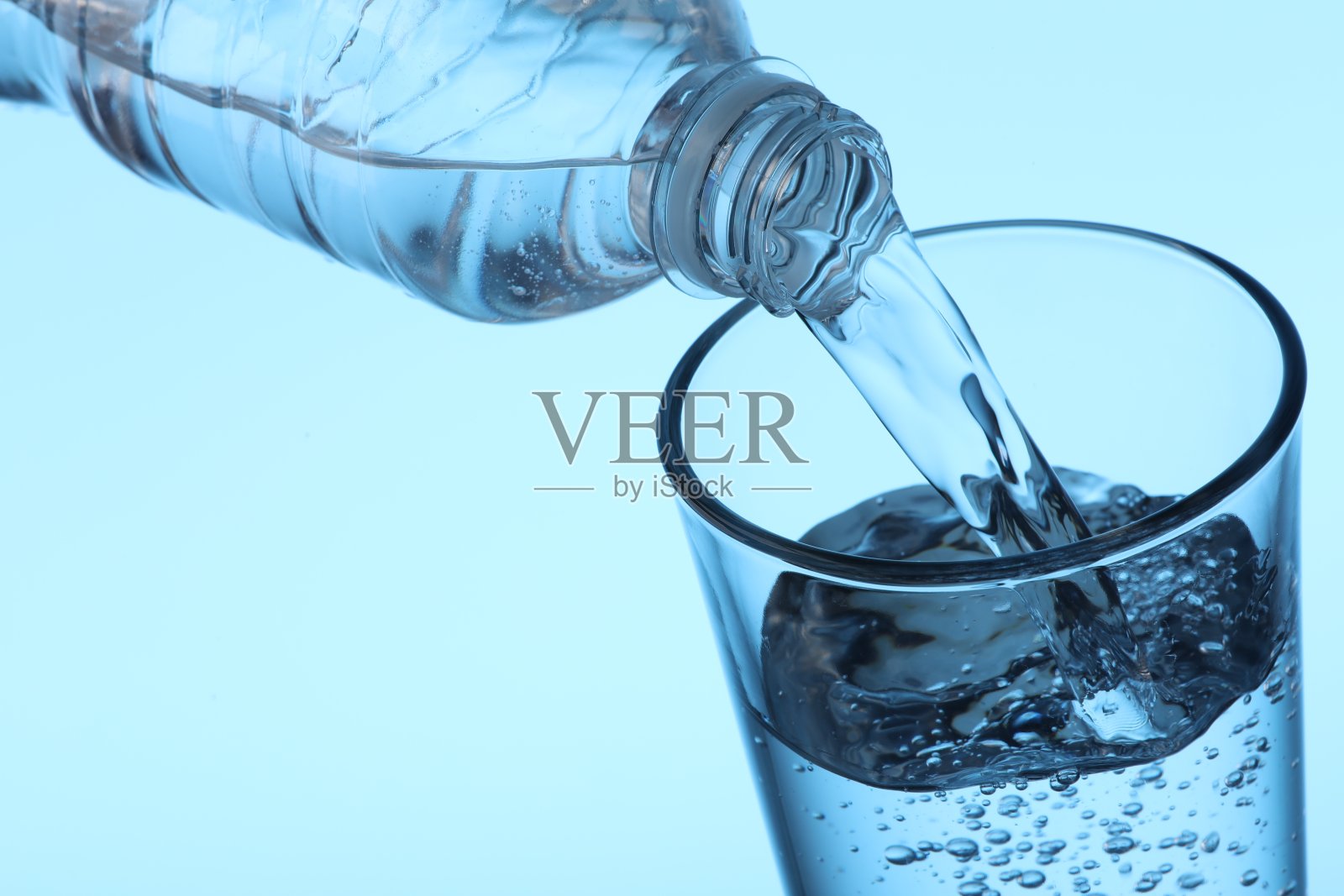 把水从瓶子倒进玻璃杯，浅蓝色背景，特写照片摄影图片
