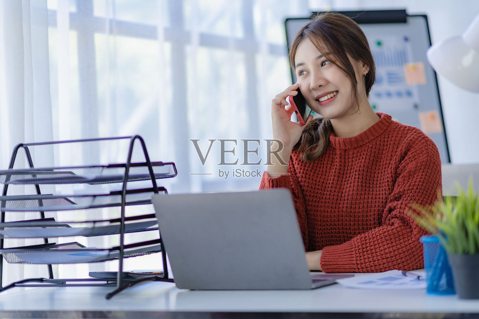 微笑的亚洲女性与客户通电话年轻积极的女会计师用智能手机与她的团队在她的办公桌上放松的移动应用程序照片摄影图片