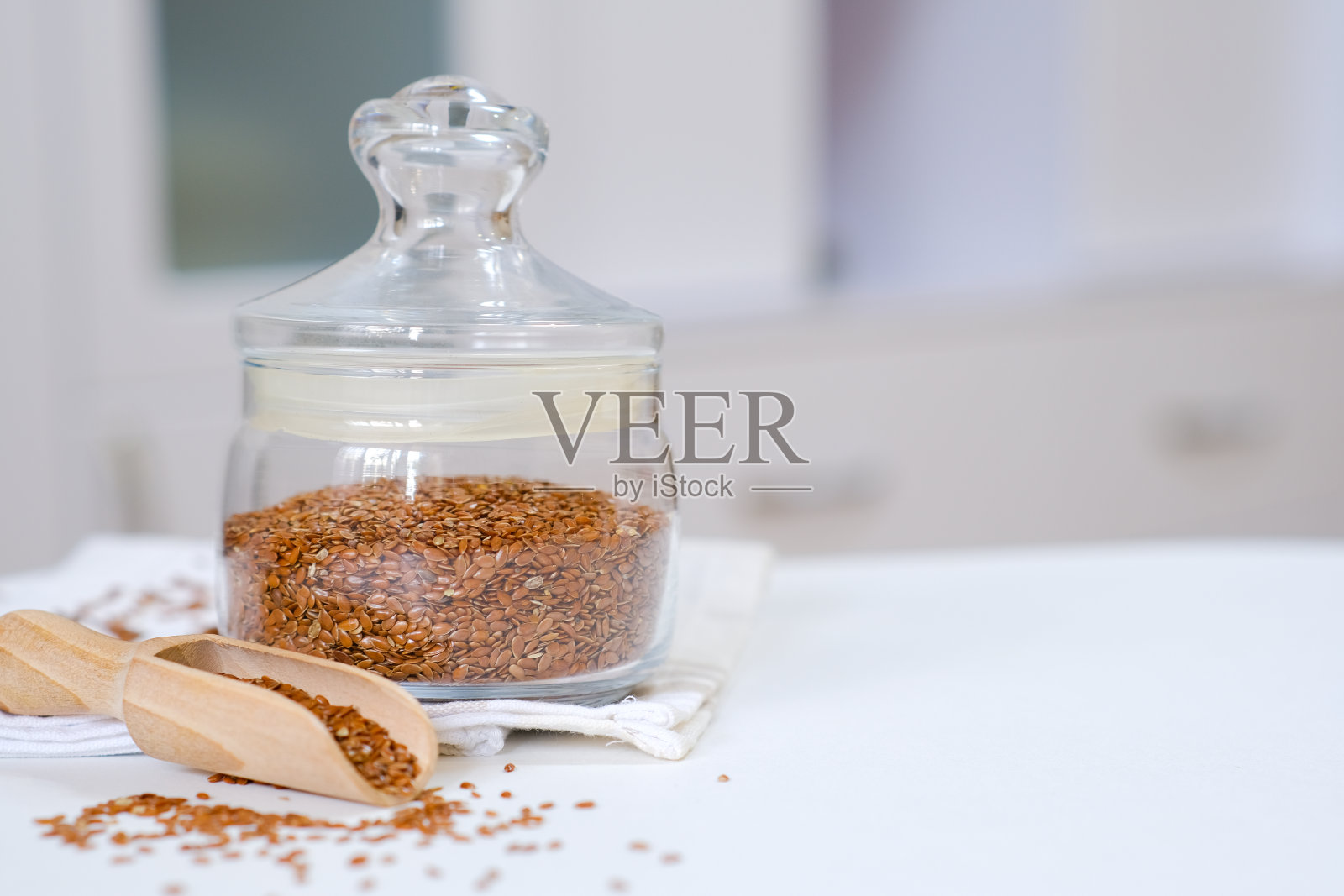 亚麻籽放在玻璃罐里，木勺放在亚麻餐巾上，厨房的白色桌子上。照片摄影图片