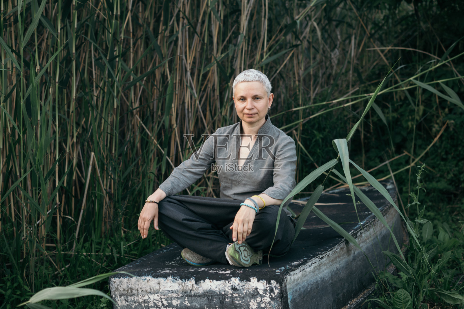 一个女人在大自然中的肖像，坐在河边一艘倾覆的船上照片摄影图片