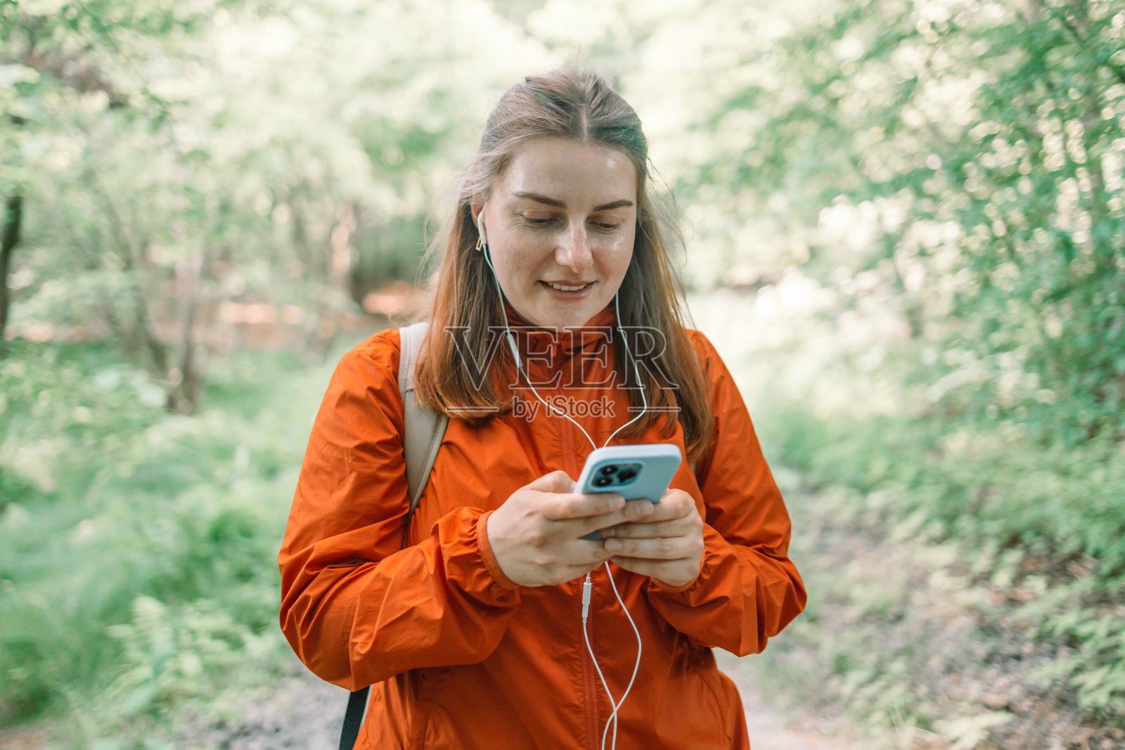 快乐的美女在森林里戴着耳机听着大自然的音乐，背着背包在夏日夕阳下的森林里。照片摄影图片