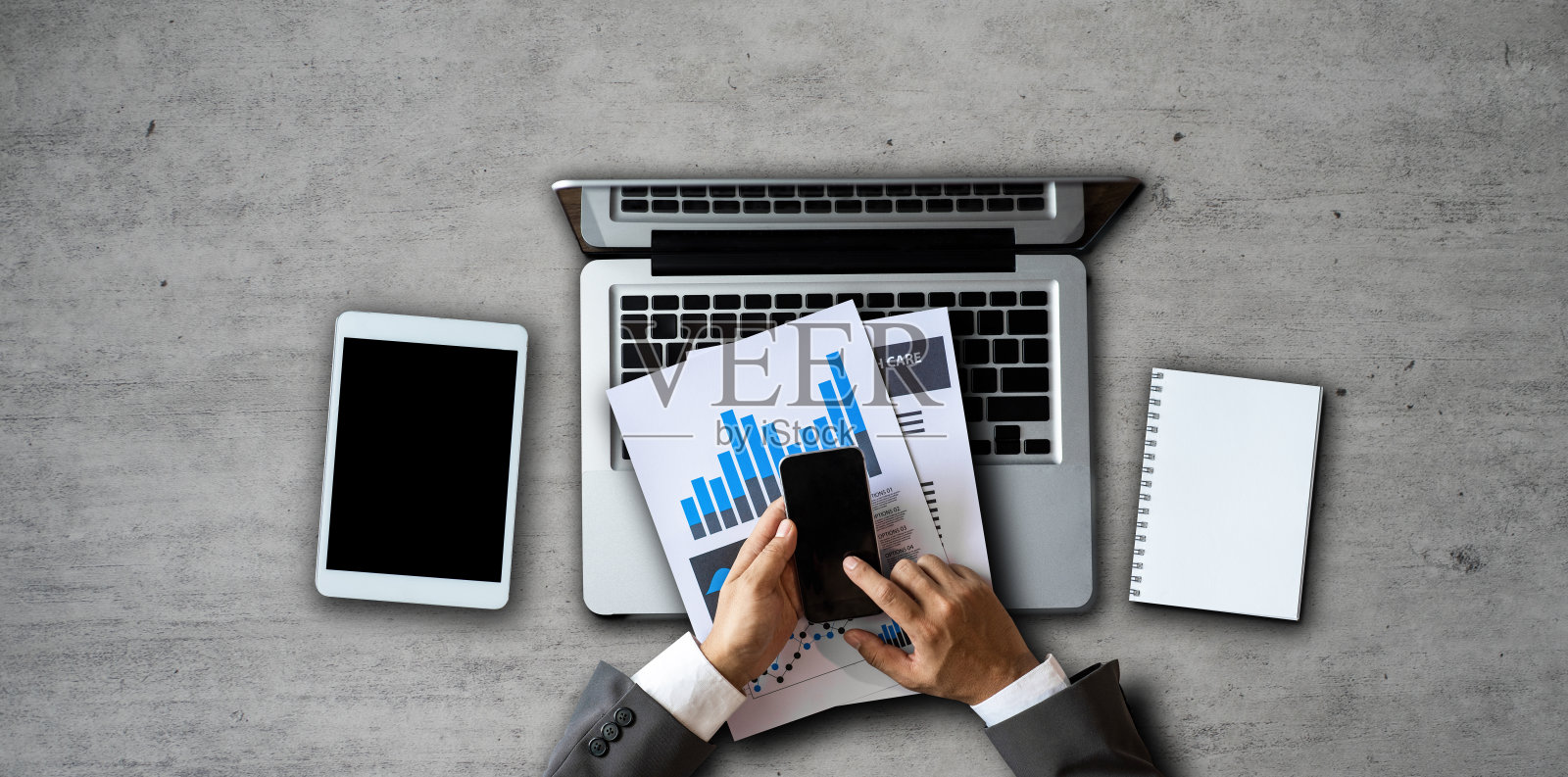 商业工作者的手拿着智能手机，平板电脑和笔记本电脑在现代办公桌上，办公用品俯视图。照片摄影图片