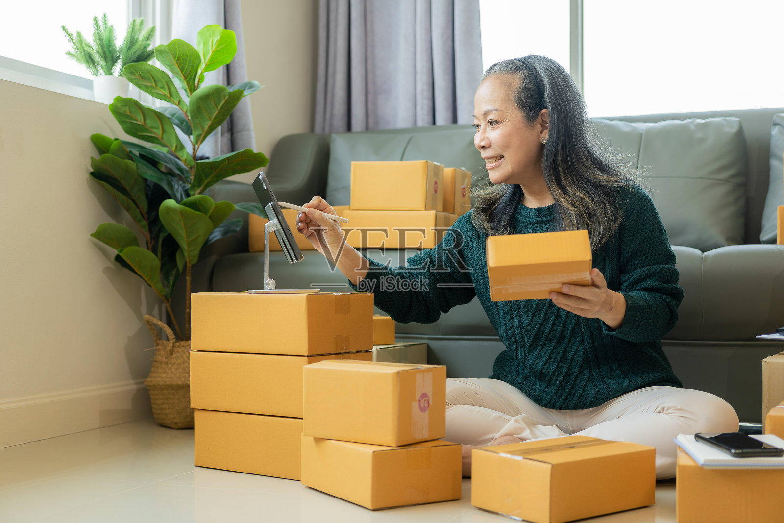 创办小型企业。成熟的老妇人双手使用智能手机或笔记本电脑平板电脑接收和验证在线订单，准备包装盒。网上购物概念照片摄影图片