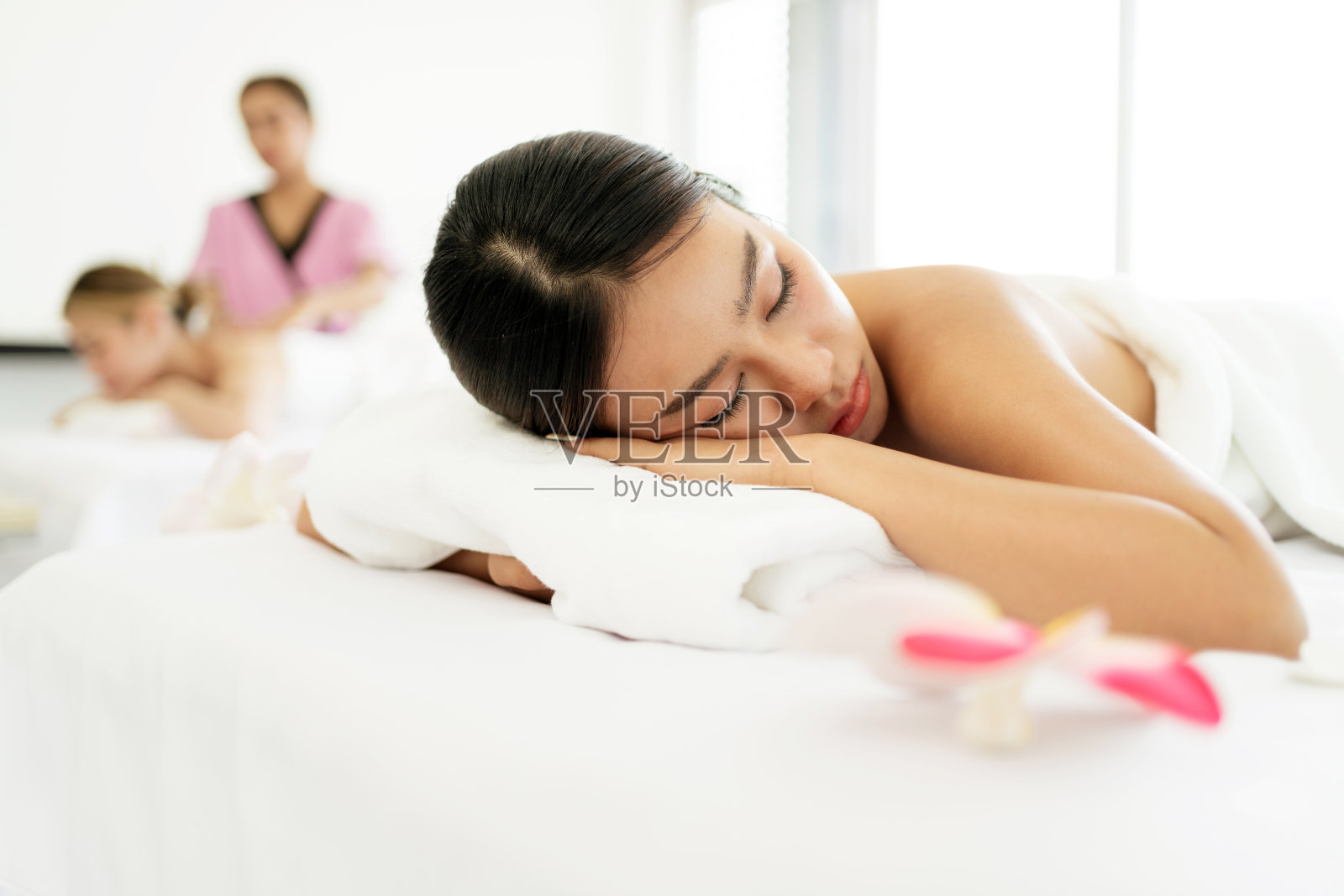 在亚洲豪华水疗沙龙的白色亚麻布和健康中心，躺在按摩床上的年轻女子闭上眼睛，等待治疗师的按摩。水疗沙龙概念照片摄影图片