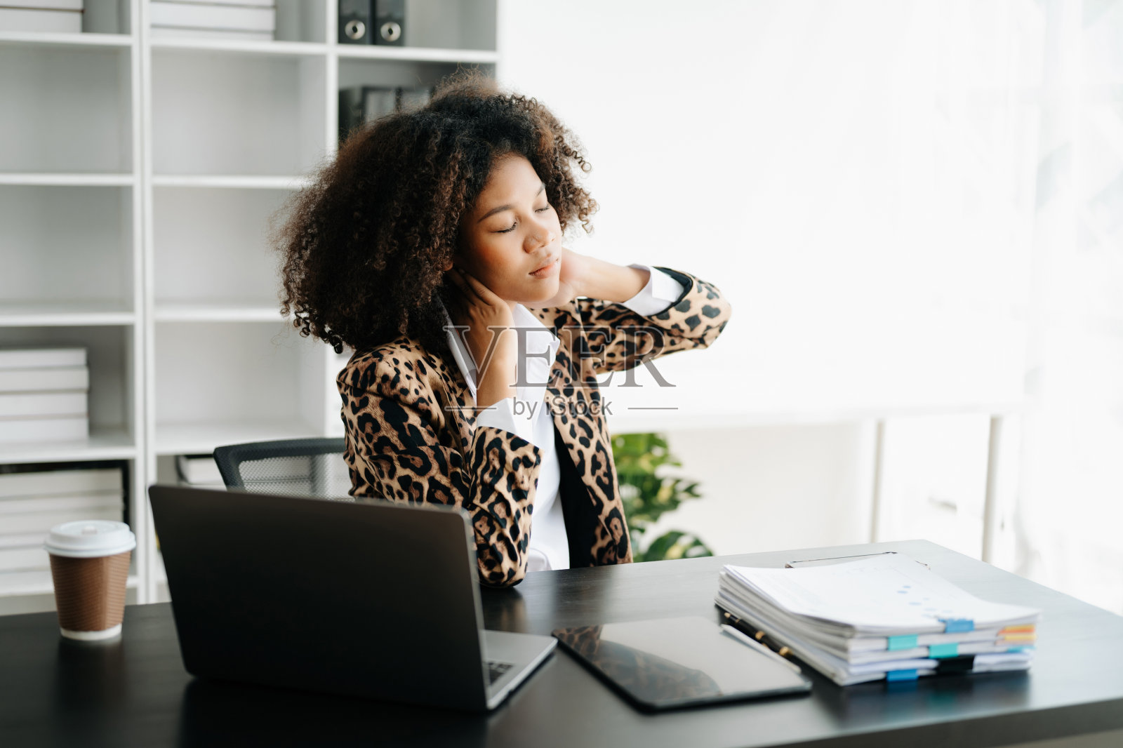 劳累过度的年轻非洲女上班族在办公桌前工作了一整天后颈部疼痛。照片摄影图片