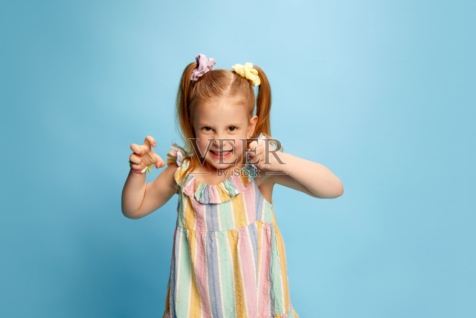 可爱，美丽，红头发的小女孩的肖像，孩子站在蓝色的工作室背景有趣的愤怒的脸。照片摄影图片