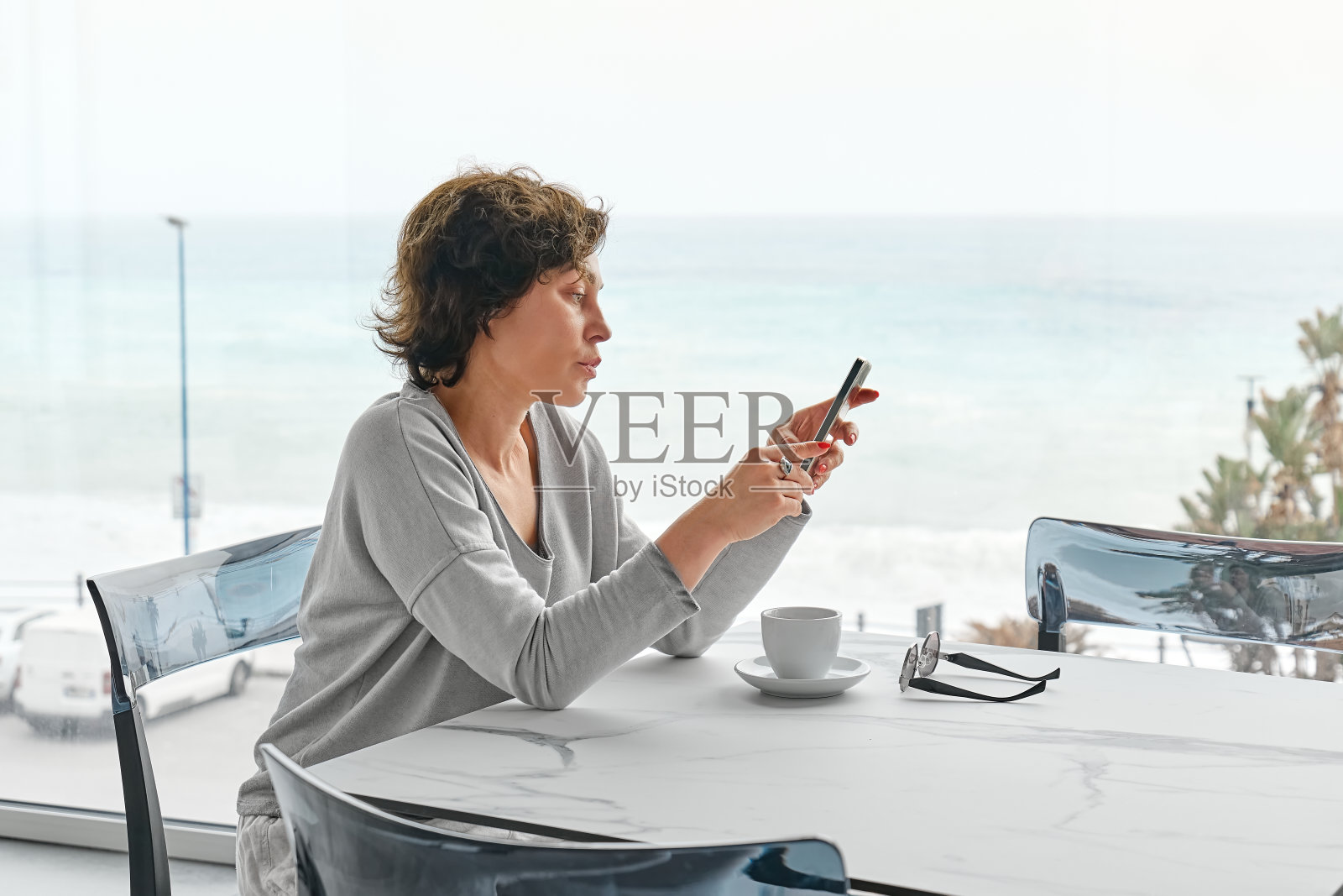 早晨，一位忧心忡忡的女子在咖啡馆里一边喝咖啡，一边查看手机社交网络。照片摄影图片