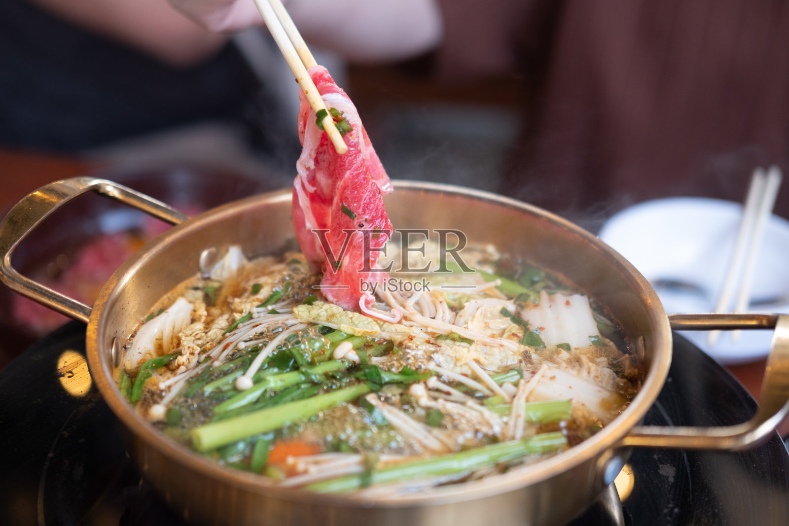 筷子夹肉片。浓汤火锅。照片摄影图片