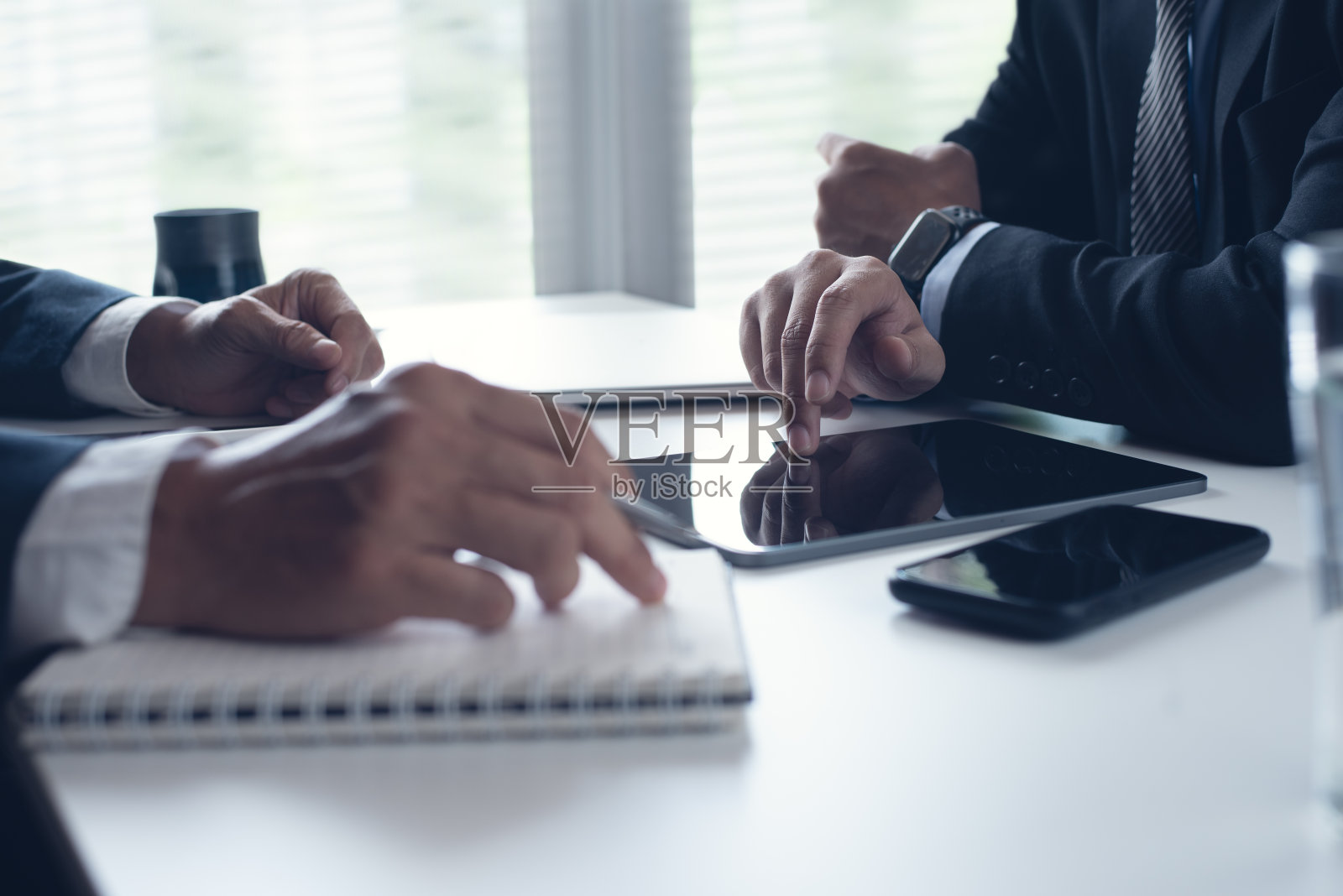 两个商人坐在桌子旁，用数码平板电脑和笔记本电脑在现代办公室里共同工作。业务同事在一起工作，讨论一个项目照片摄影图片