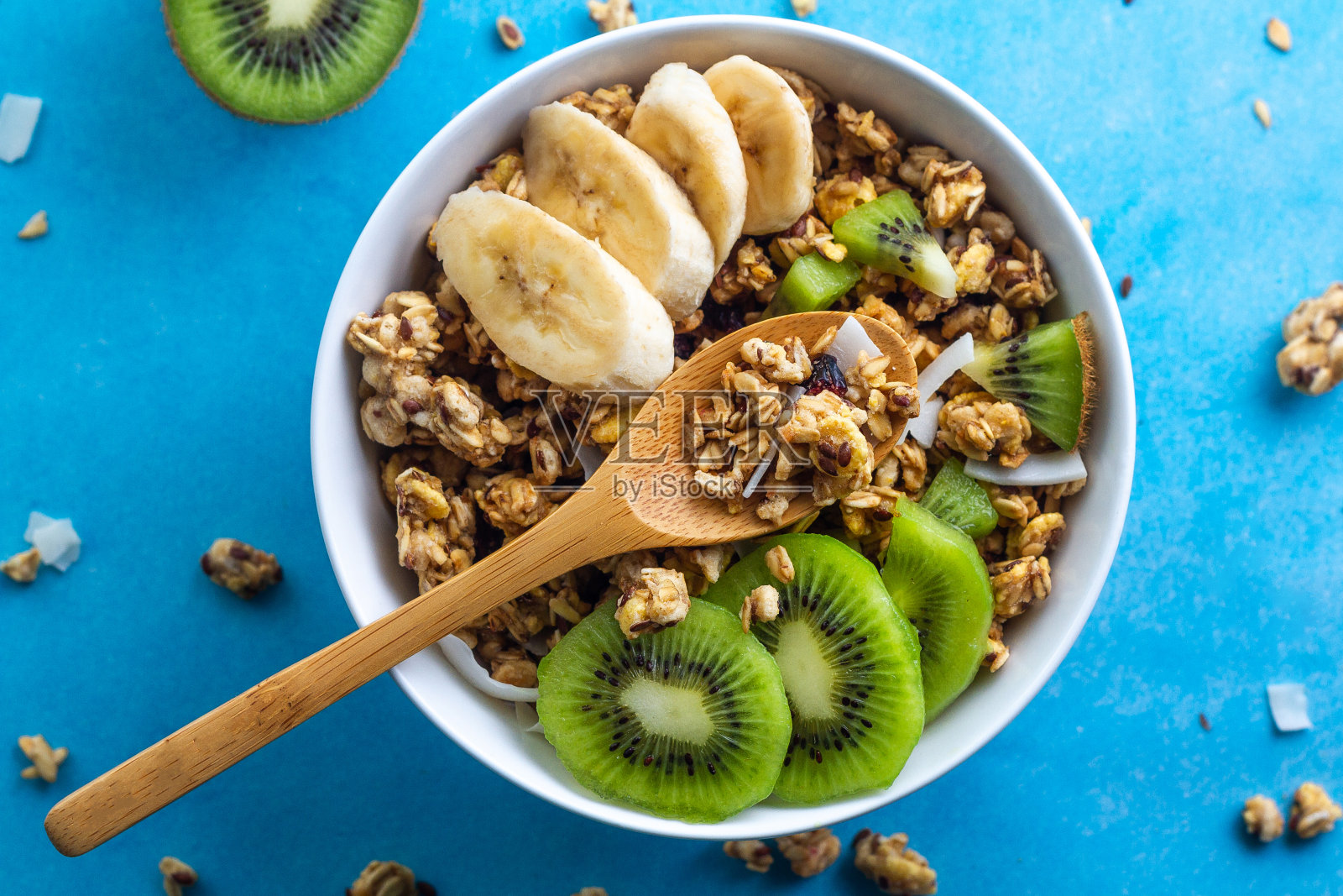 干早餐麦片。清脆的蜂蜜什锦碗配上新鲜的香蕉片和蓝色背景的猕猴桃。健康，健身和纤维食物。前视图。早餐时间照片摄影图片