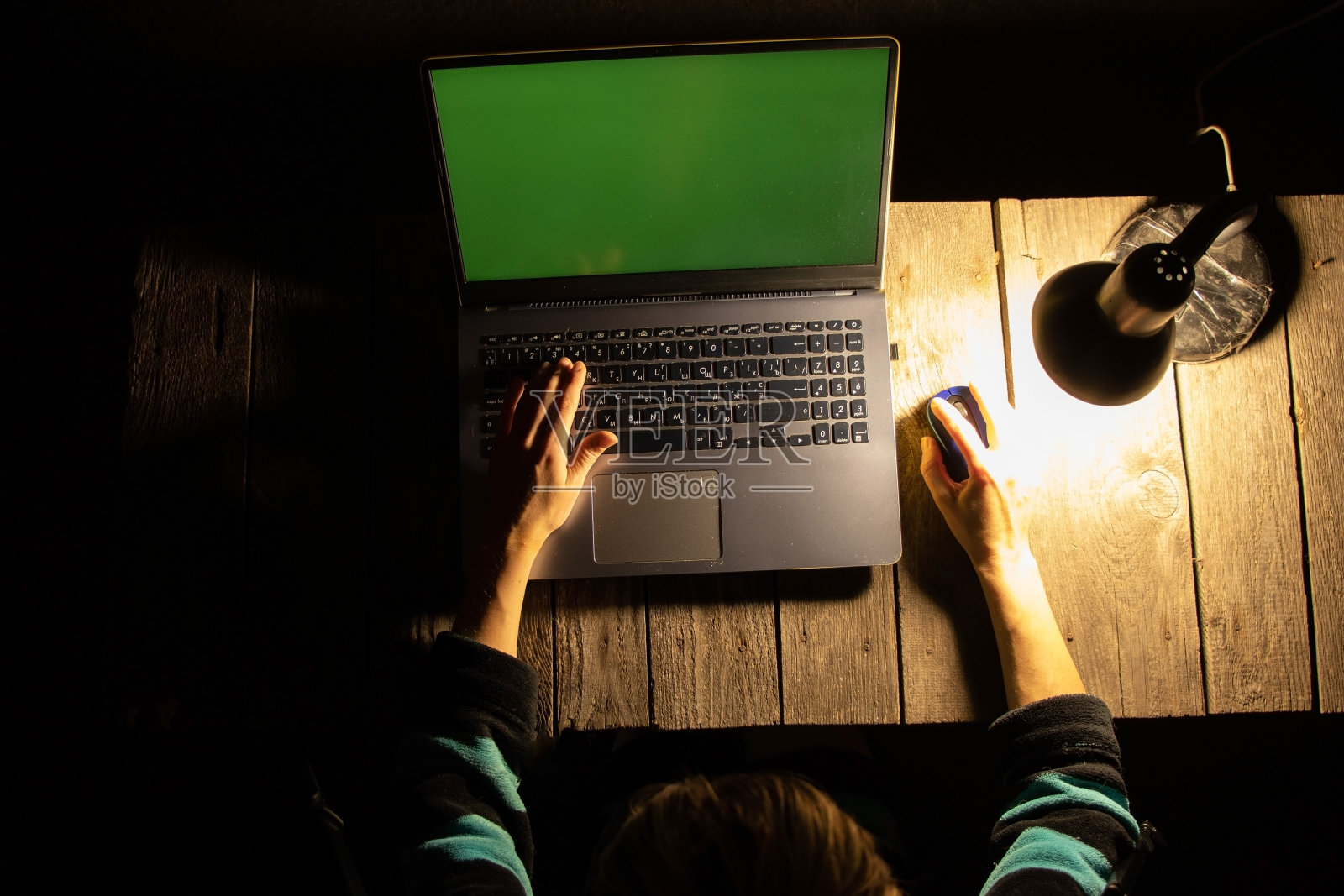 一个女孩在黑暗中坐在家里桌子旁的一盏灯旁的笔记本电脑前照片摄影图片