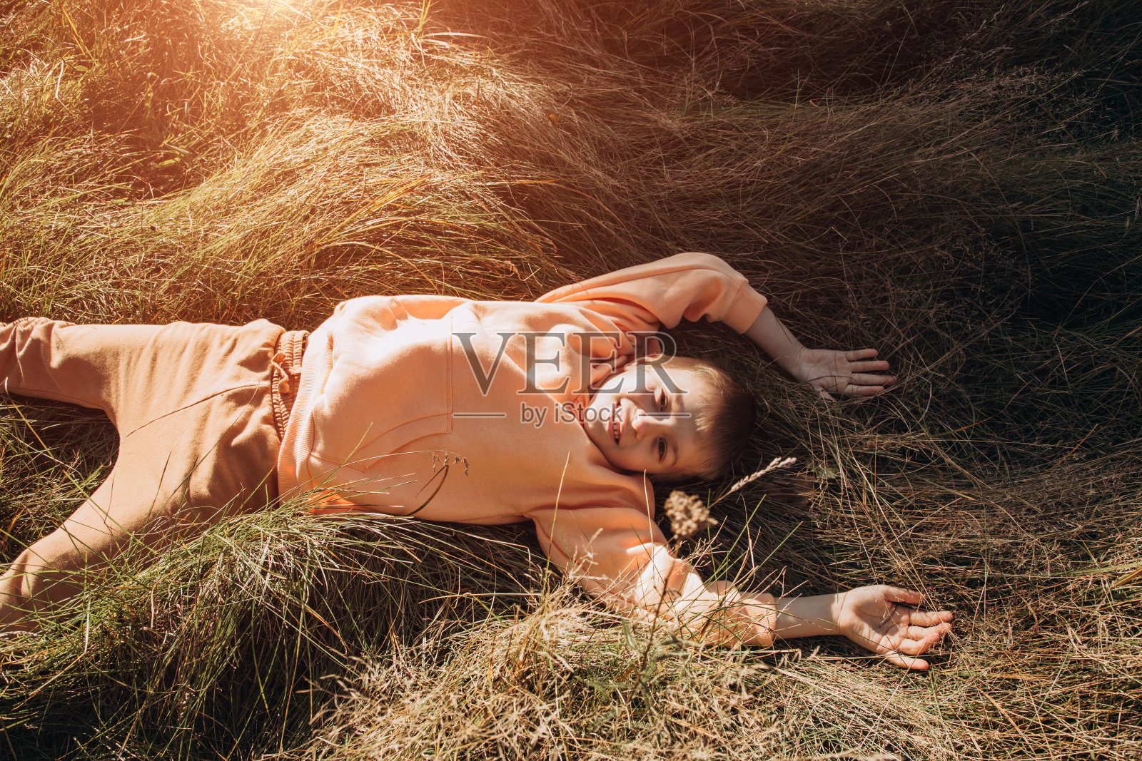 一个快乐的男孩躺在草地上高高的草地上。公园户外休闲照片摄影图片