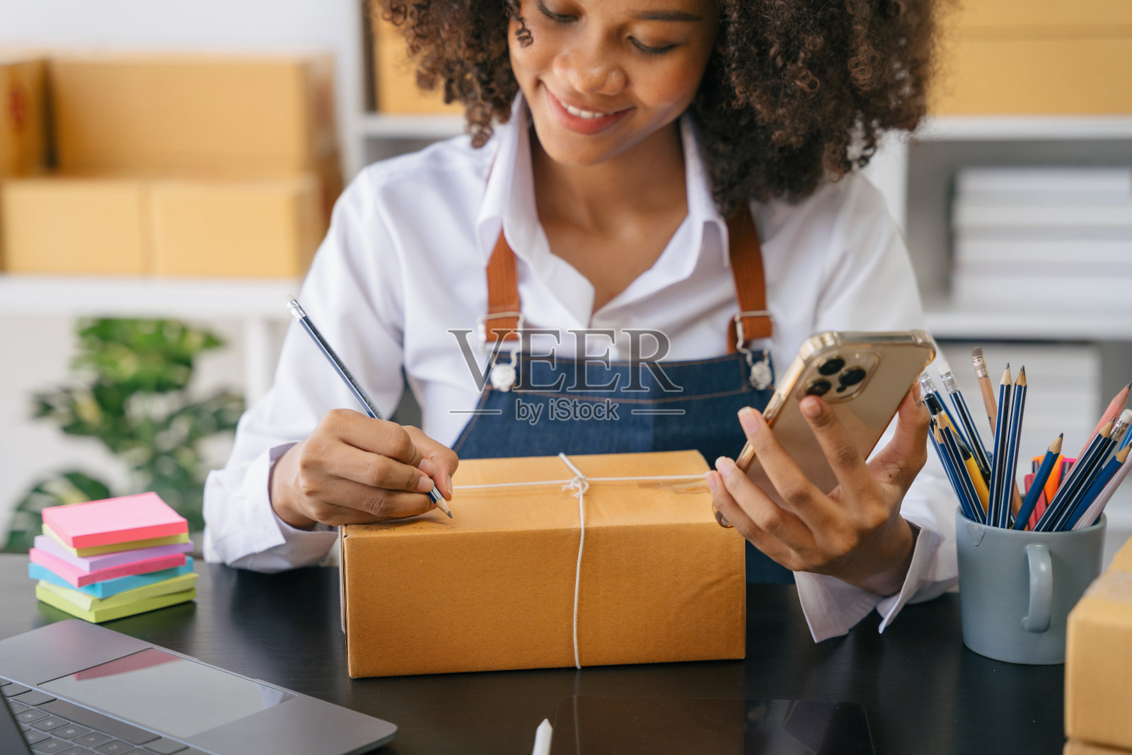网上送货购物，女性创业小企业主在工作场所的纸板箱上写地址。小型企业的企业家或自由职业的亚洲妇女在家里做盒子。照片摄影图片