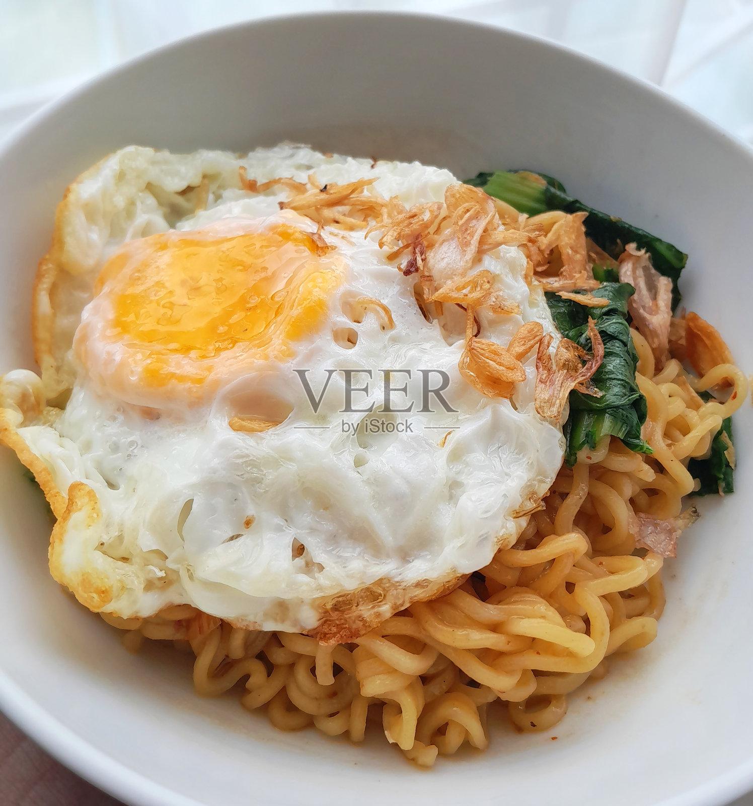 印尼美食:速食Indomie Mi Goreng配小白菜蔬菜，煎蛋，上面撒上霸王Goreng。照片摄影图片