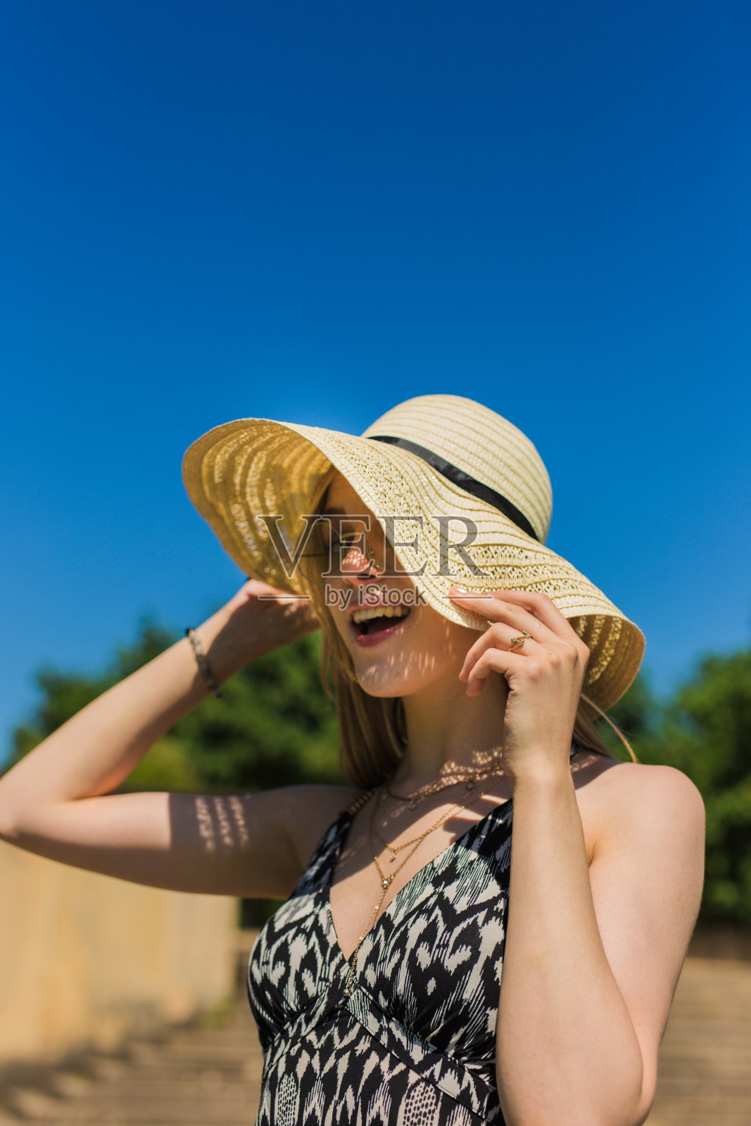在一个阳光明媚的日子里，戴着帽子的快乐的女人站在海滩上笑着照片摄影图片