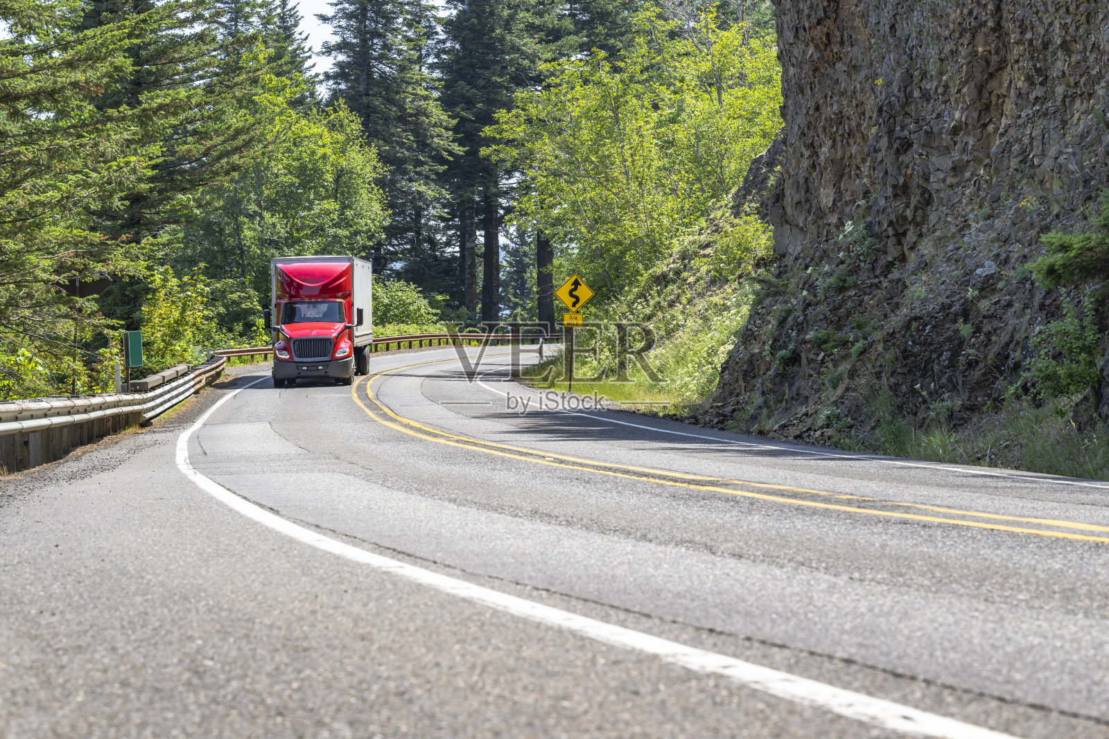 专业工业大钻机高驾驶室红色半挂车，干式货车半挂车运输货物，行驶在森林和岩石的弯曲山路上照片摄影图片