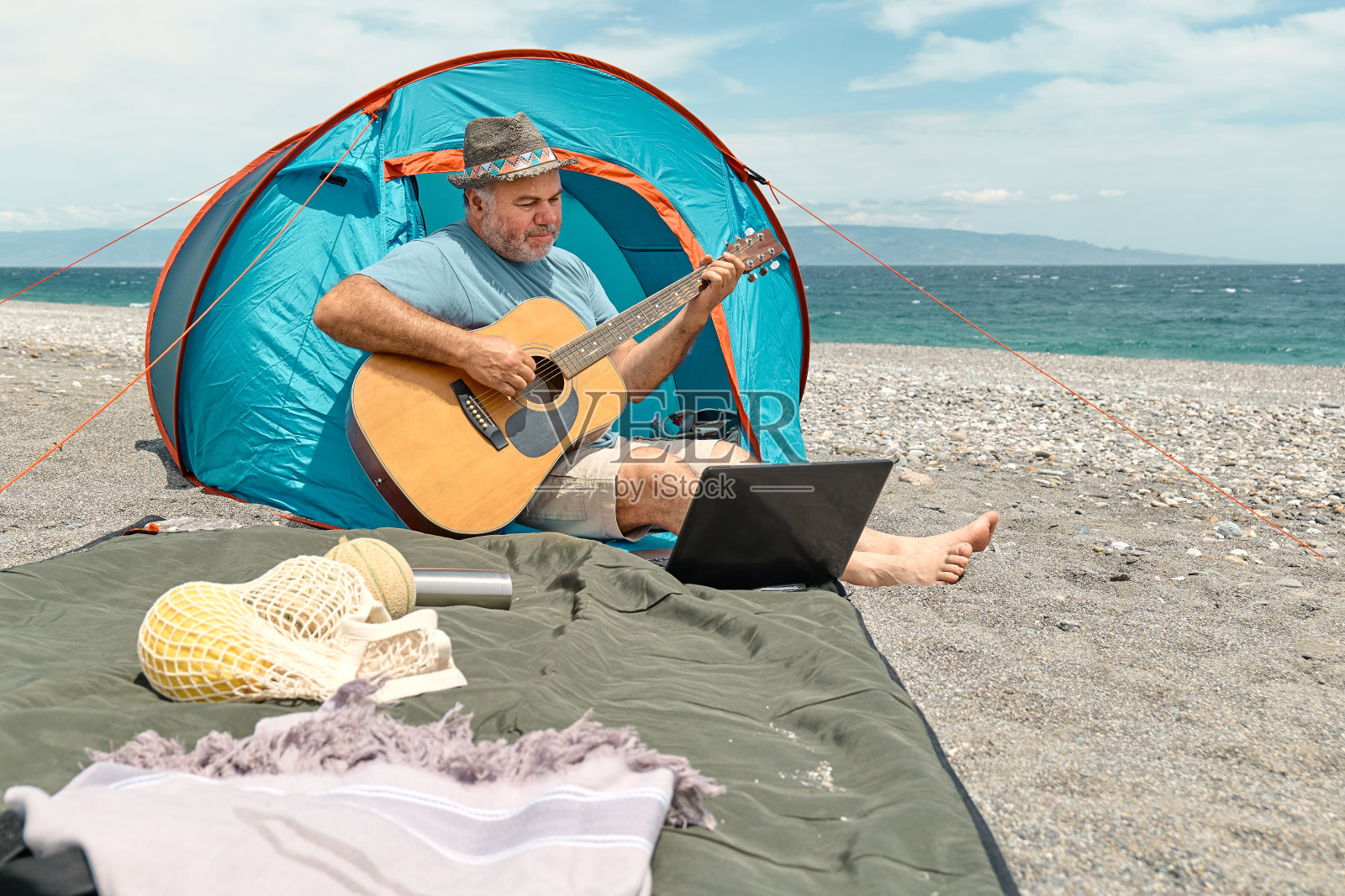暑假在海边露营野餐的中年大胡子男子一边弹吉他一边唱歌。照片摄影图片