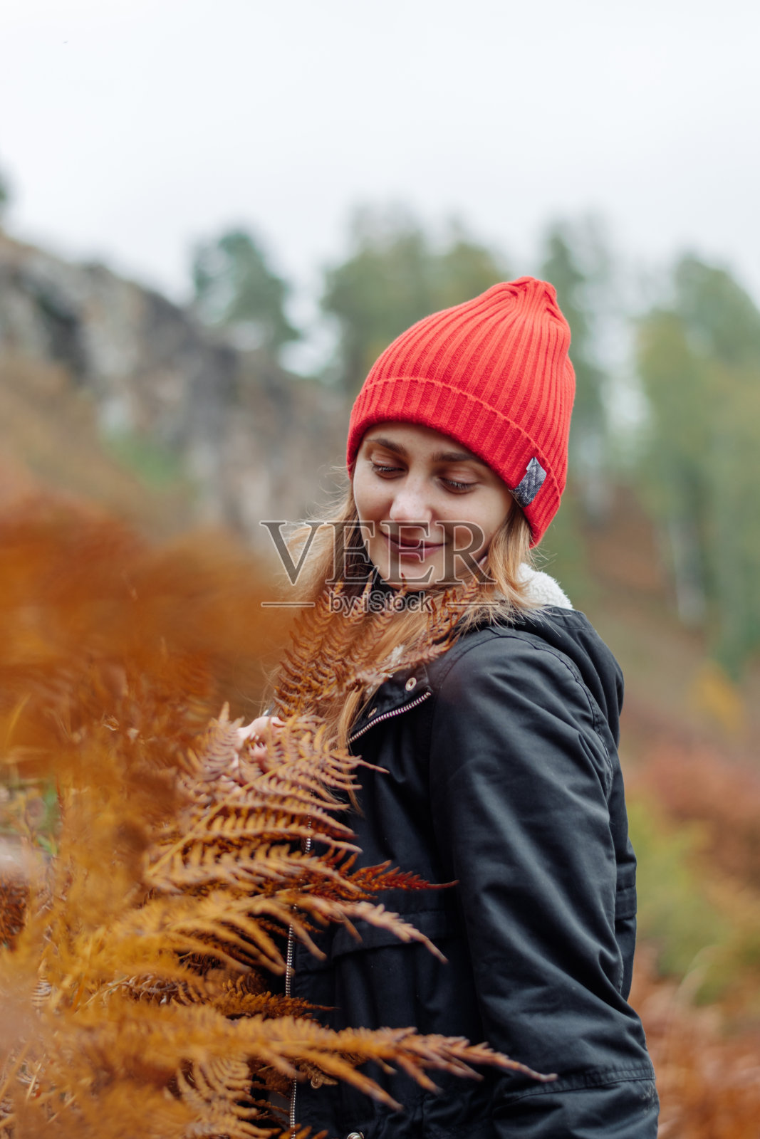 一位快乐的年轻女子走过一片黄色蕨类植物的田野，欣赏着景色。秋天，旅行，户外探险，慢生活理念照片摄影图片