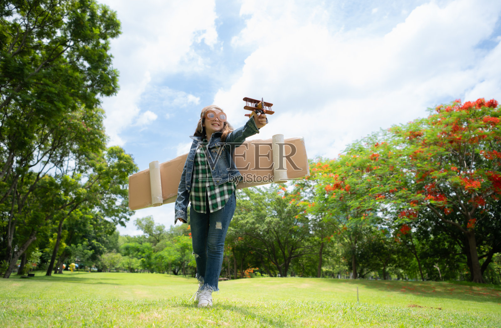 一个在公园度假的小女孩穿着飞行员的衣服和飞行设备。到处跑，和她的梦想玩得开心。照片摄影图片