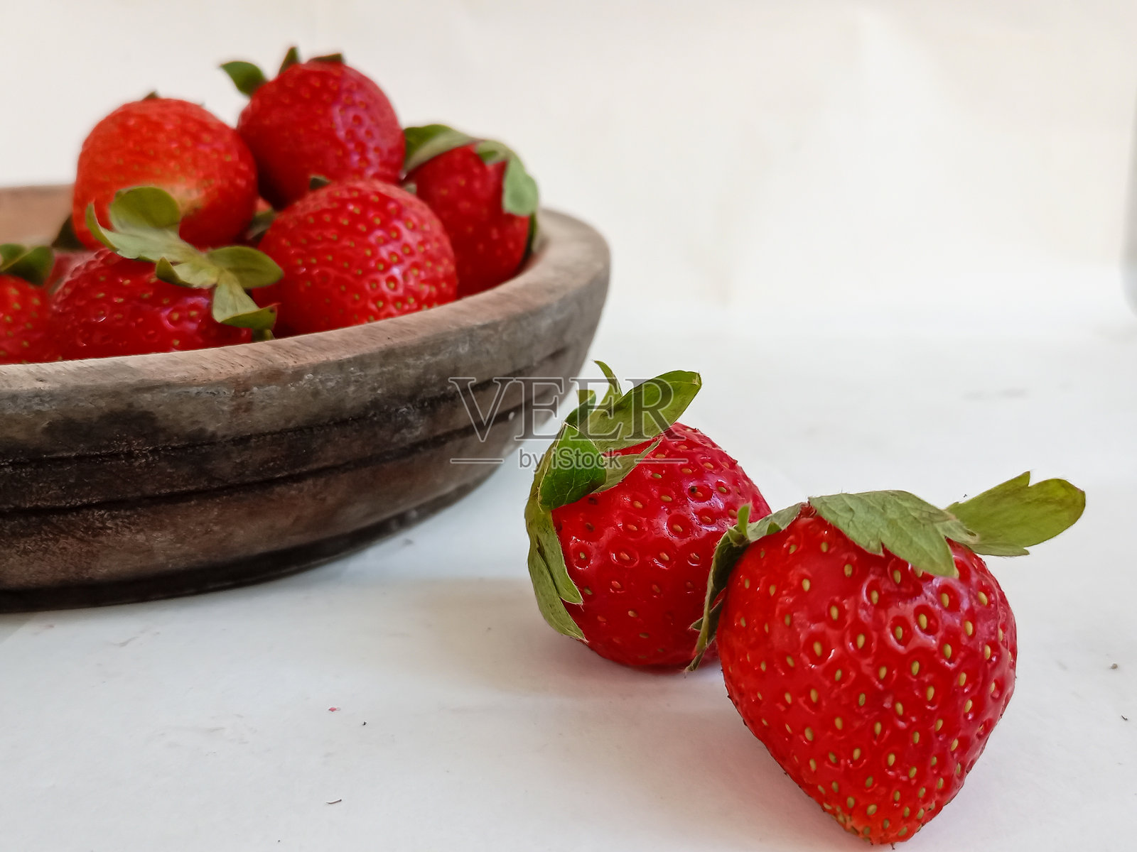 白底木碗里的一堆新鲜草莓。照片摄影图片