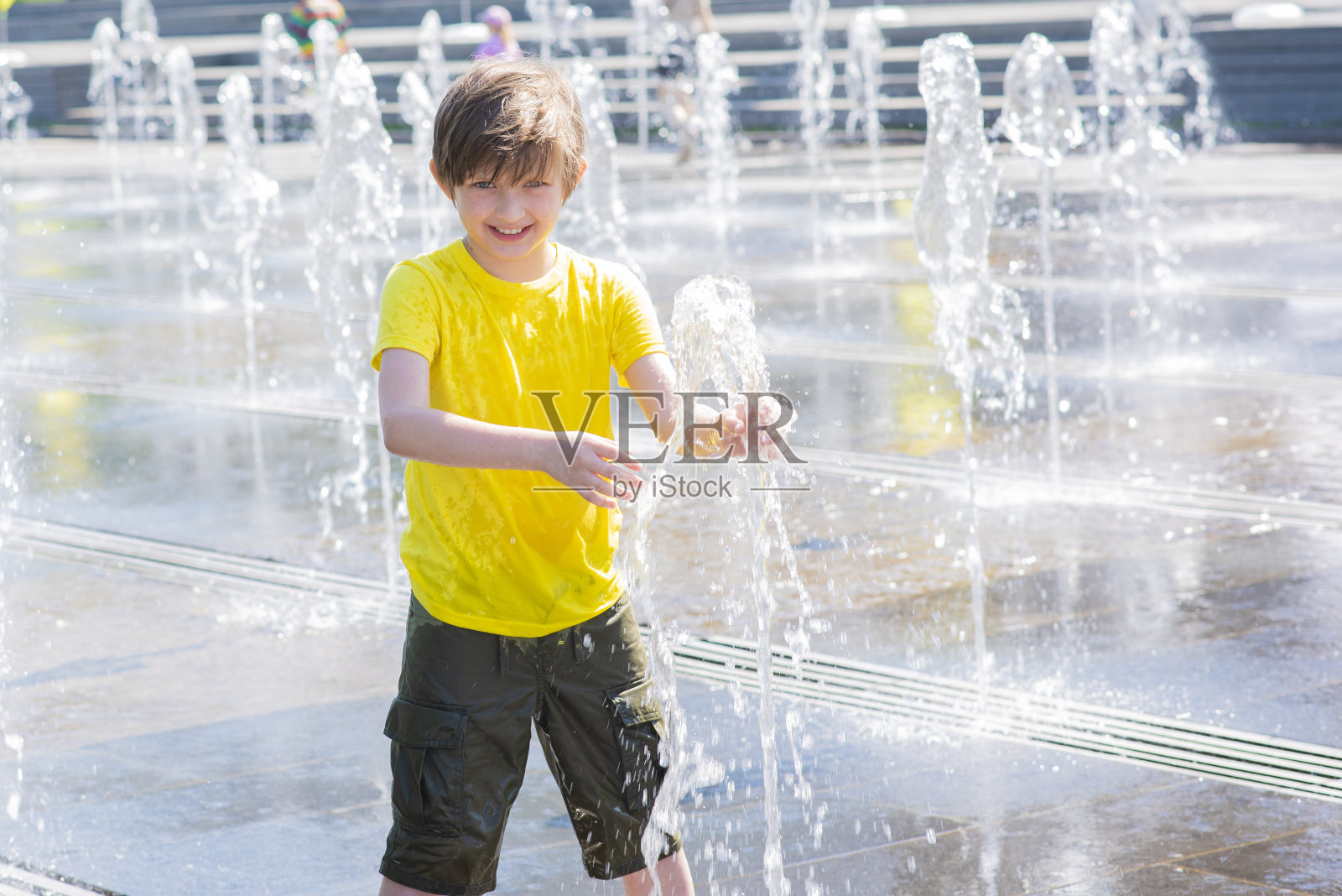 快乐的孩子在干涸的喷泉里玩耍。喷泉里快乐微笑的湿男孩照片摄影图片