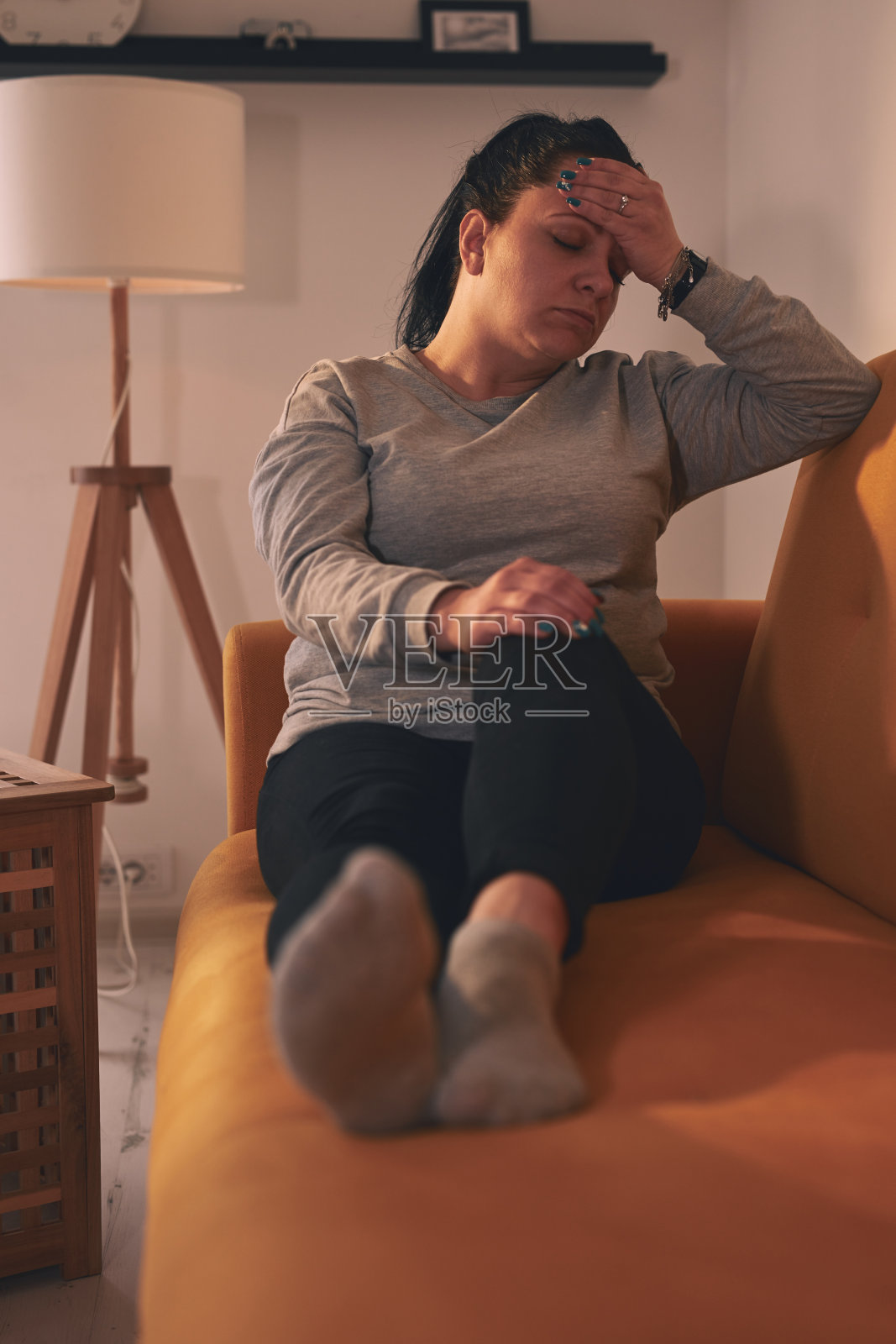头痛的女人坐在家里的沙发上。照片摄影图片