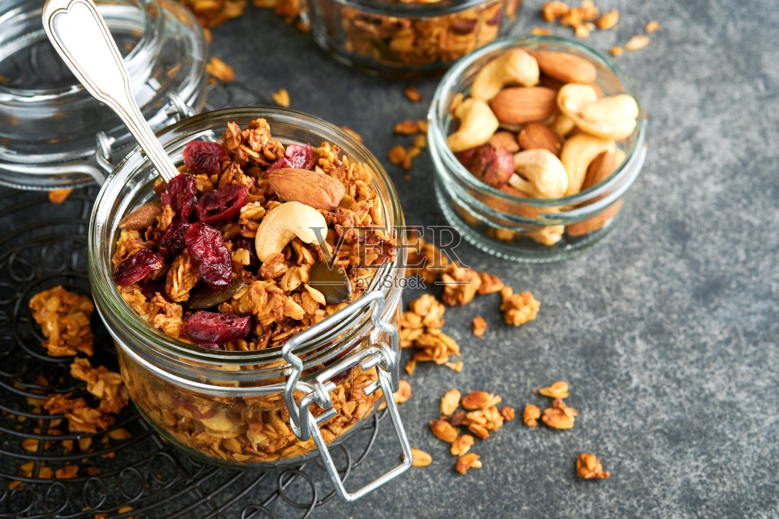 自制格兰诺拉麦片装在玻璃罐里，搭配希腊酸奶或牛奶、腰果、杏仁、南瓜和干蔓越莓籽，深灰色的餐桌背景。健康的能量早餐或零食。俯视图照片摄影图片