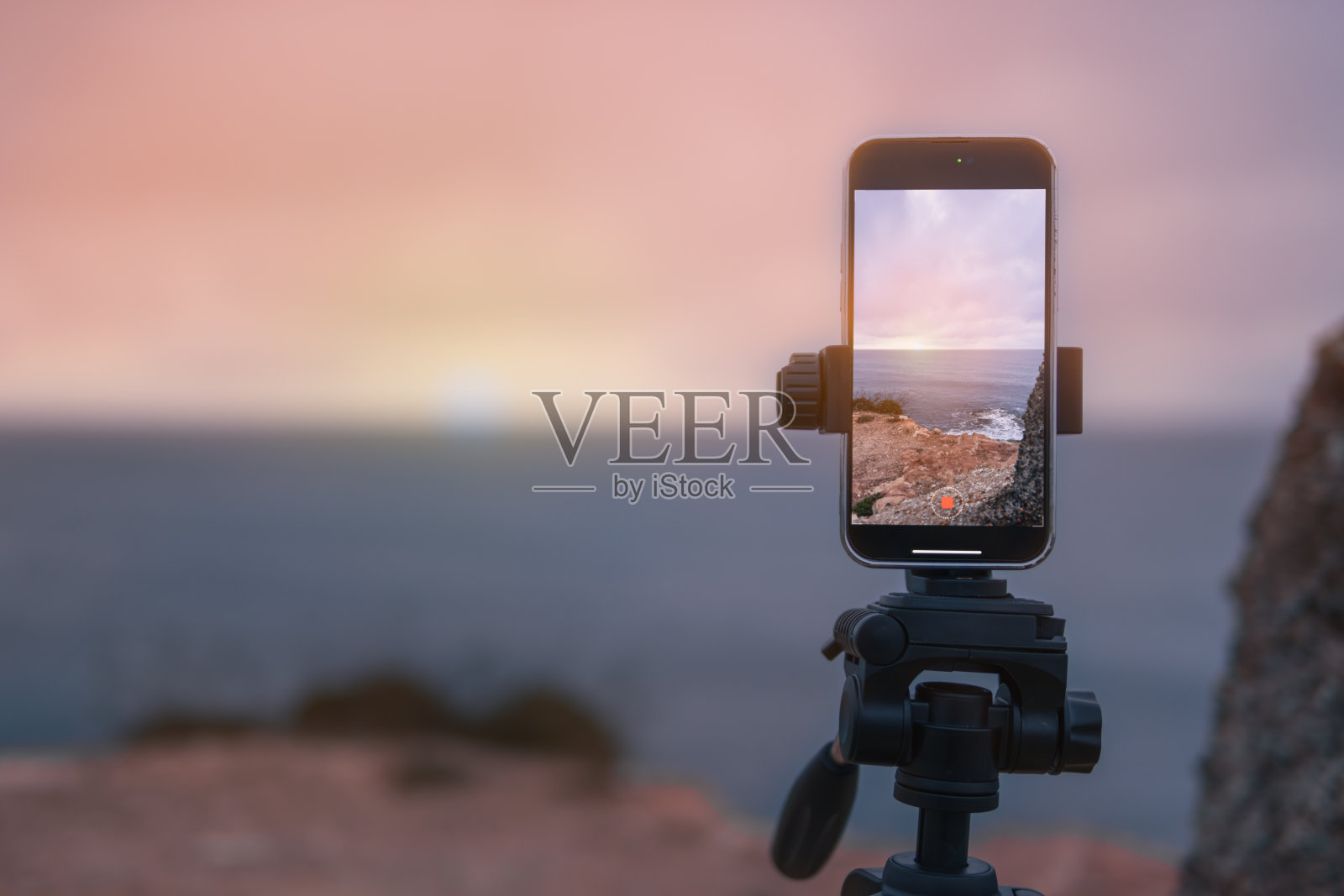 黎明时分，三脚架上的手机立在海边的山上，拍摄着黎明的景色。美丽的海景在电话特写上有一席之地照片摄影图片