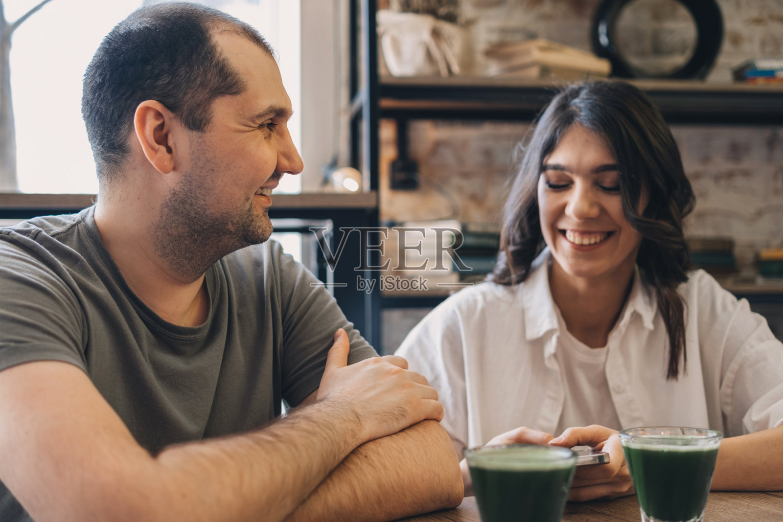 一个快乐的男人和一个女人在咖啡馆里聊天。桌上有几杯抹茶。沟通，健康饮食理念照片摄影图片