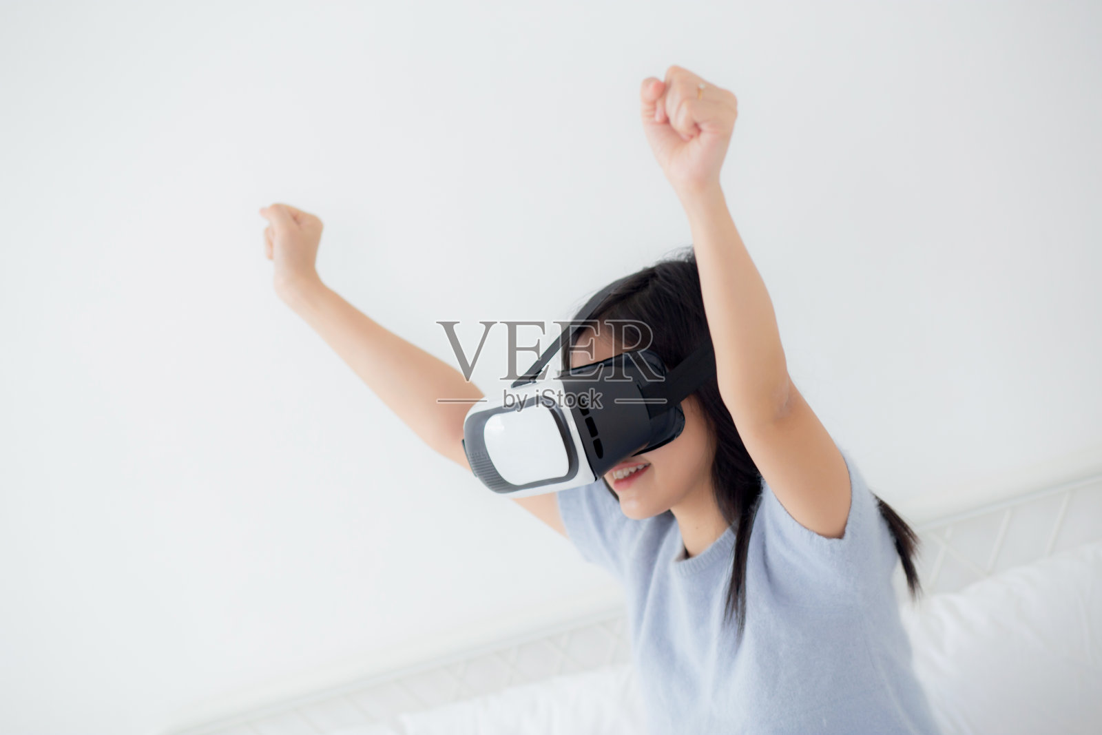 年轻的亚洲女性戴着vr耳机在家里的卧室里兴奋地玩游戏，女性利用虚拟现实或虚拟世界创新模拟3D，生活方式和科技概念。照片摄影图片