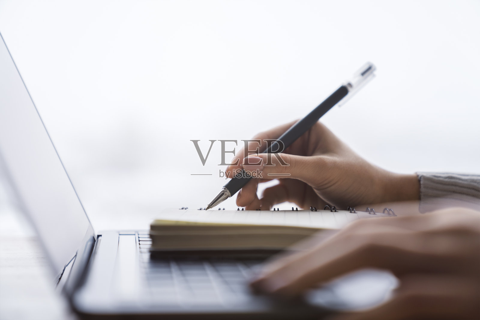 近景中，在朦胧的背景下，一个女人的手在笔记本电脑的记事本上写着笔记照片摄影图片